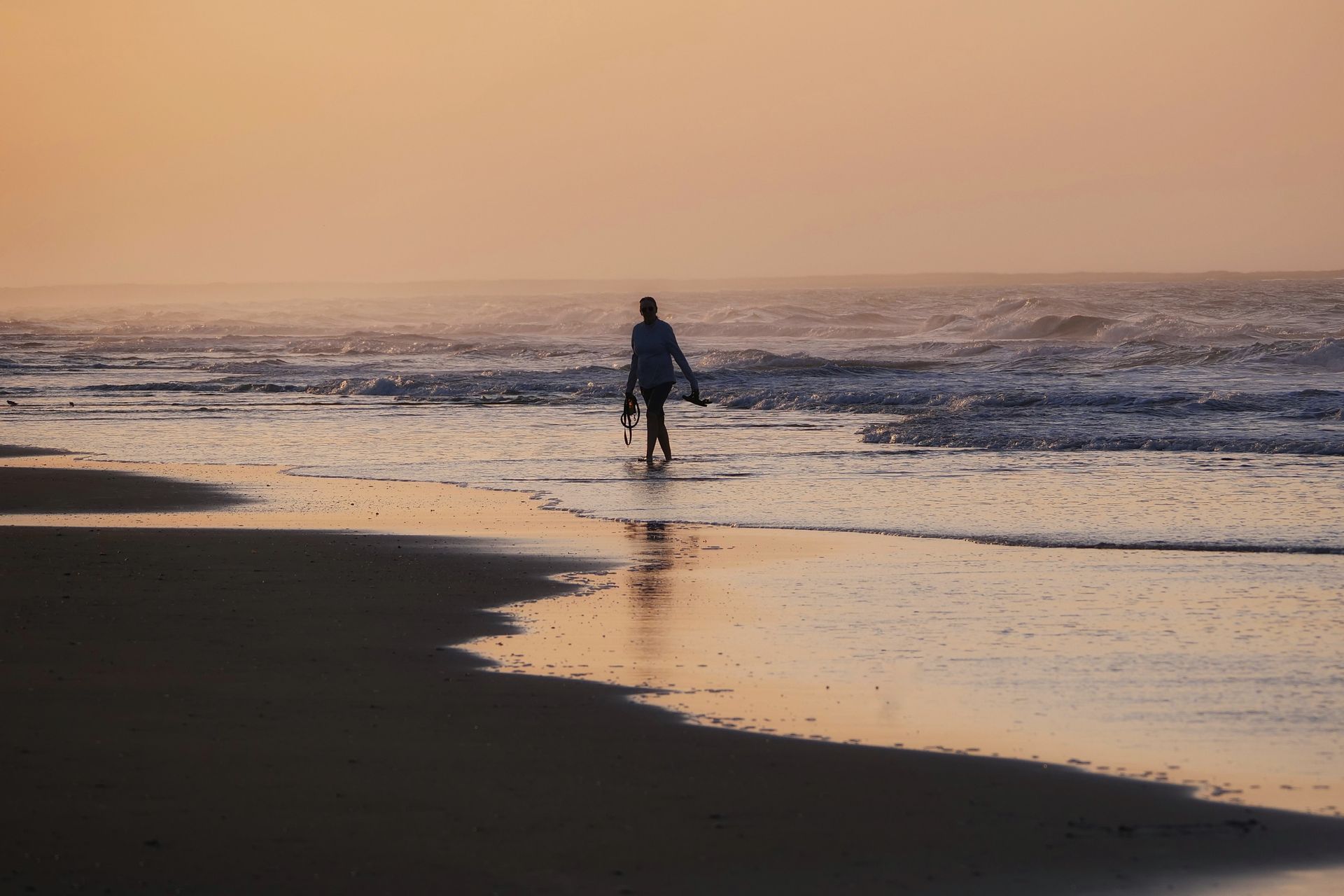 A man is walking along the beach carrying a surfboard.