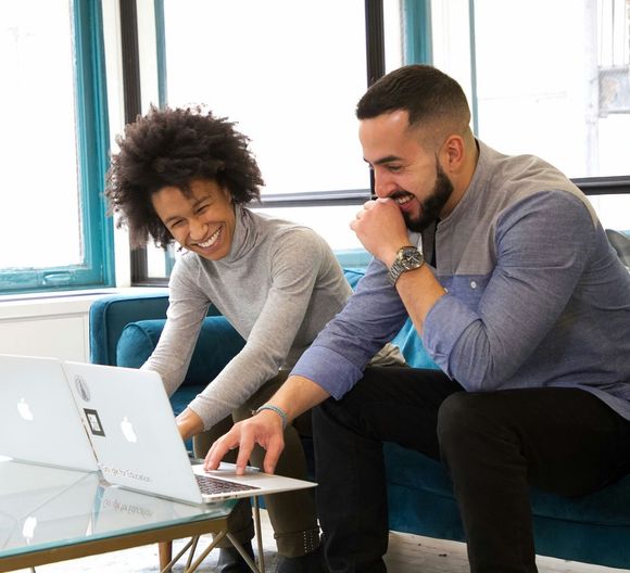 A man and a woman are sitting on a couch looking at a laptop.