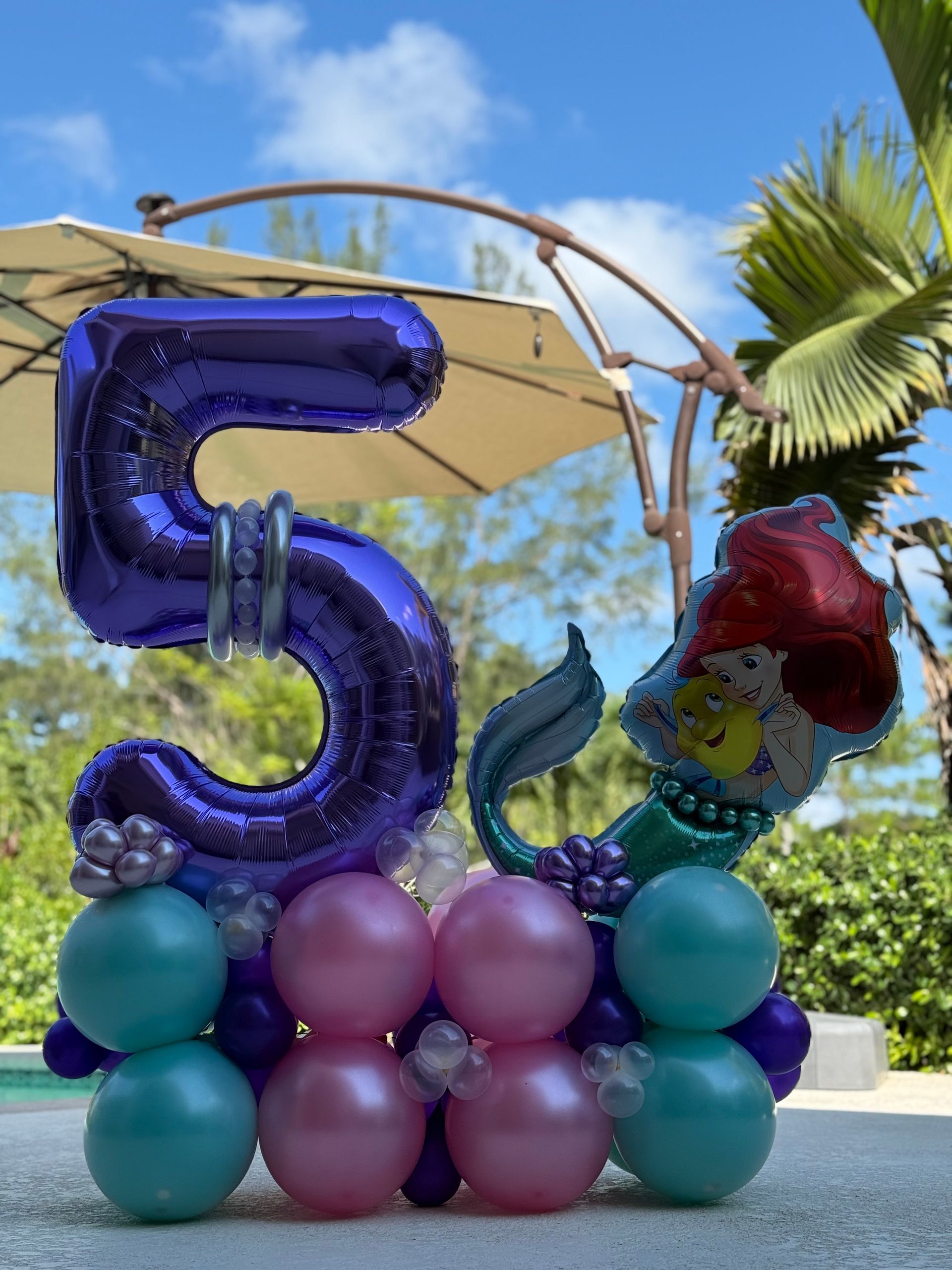 A purple number 5 balloon is surrounded by pink and green balloons.