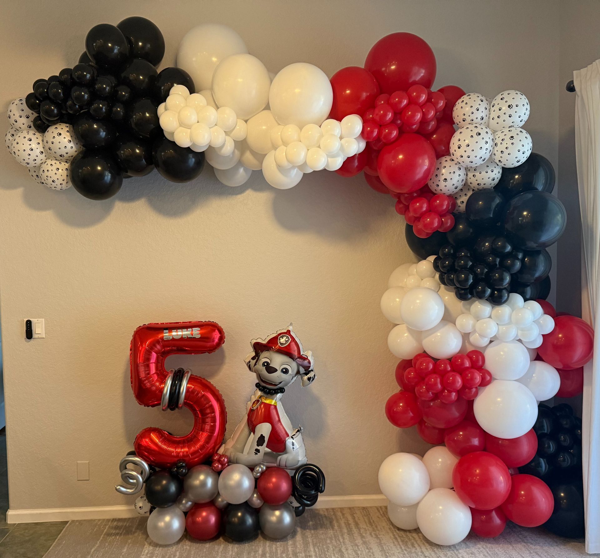A number 5 balloon is surrounded by red black and white balloons