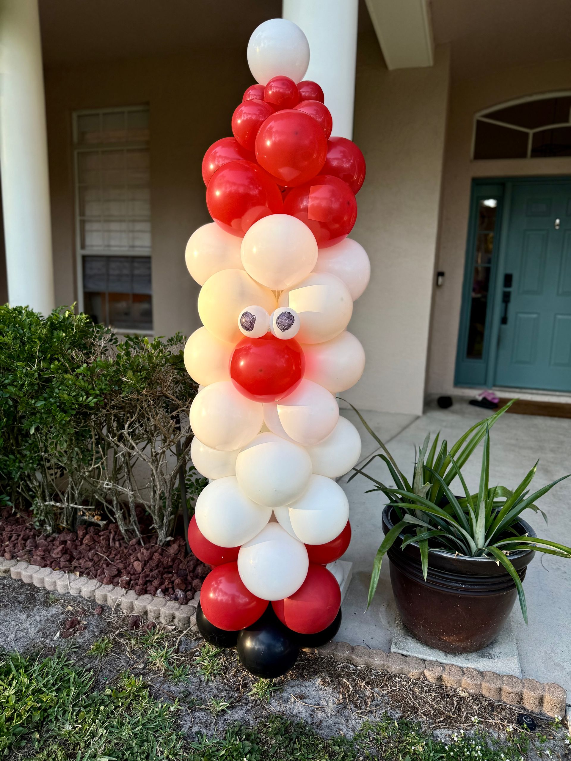 A balloon sculpture of santa claus is sitting in front of a house.