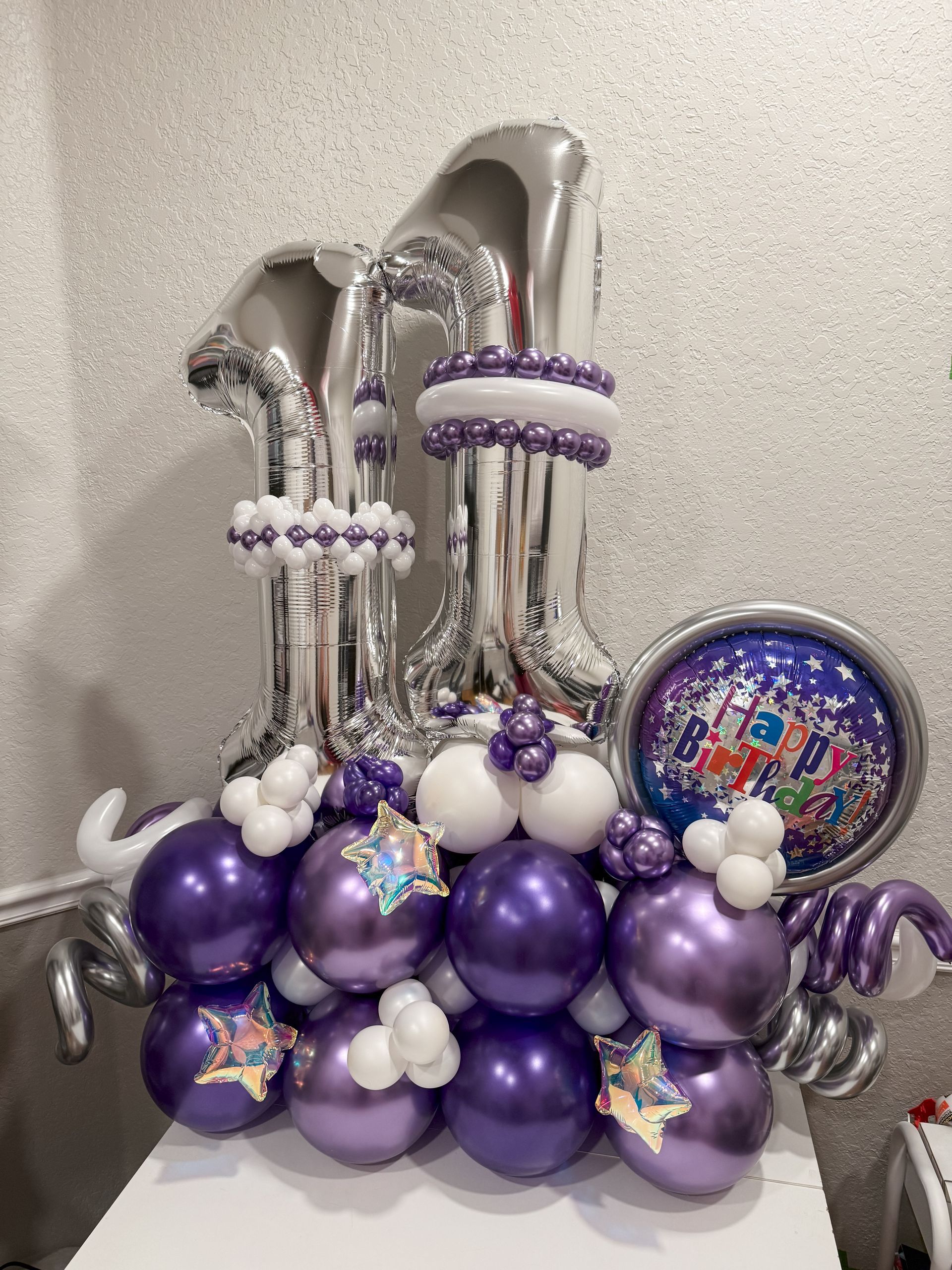A bunch of purple and silver balloons are sitting on a table.