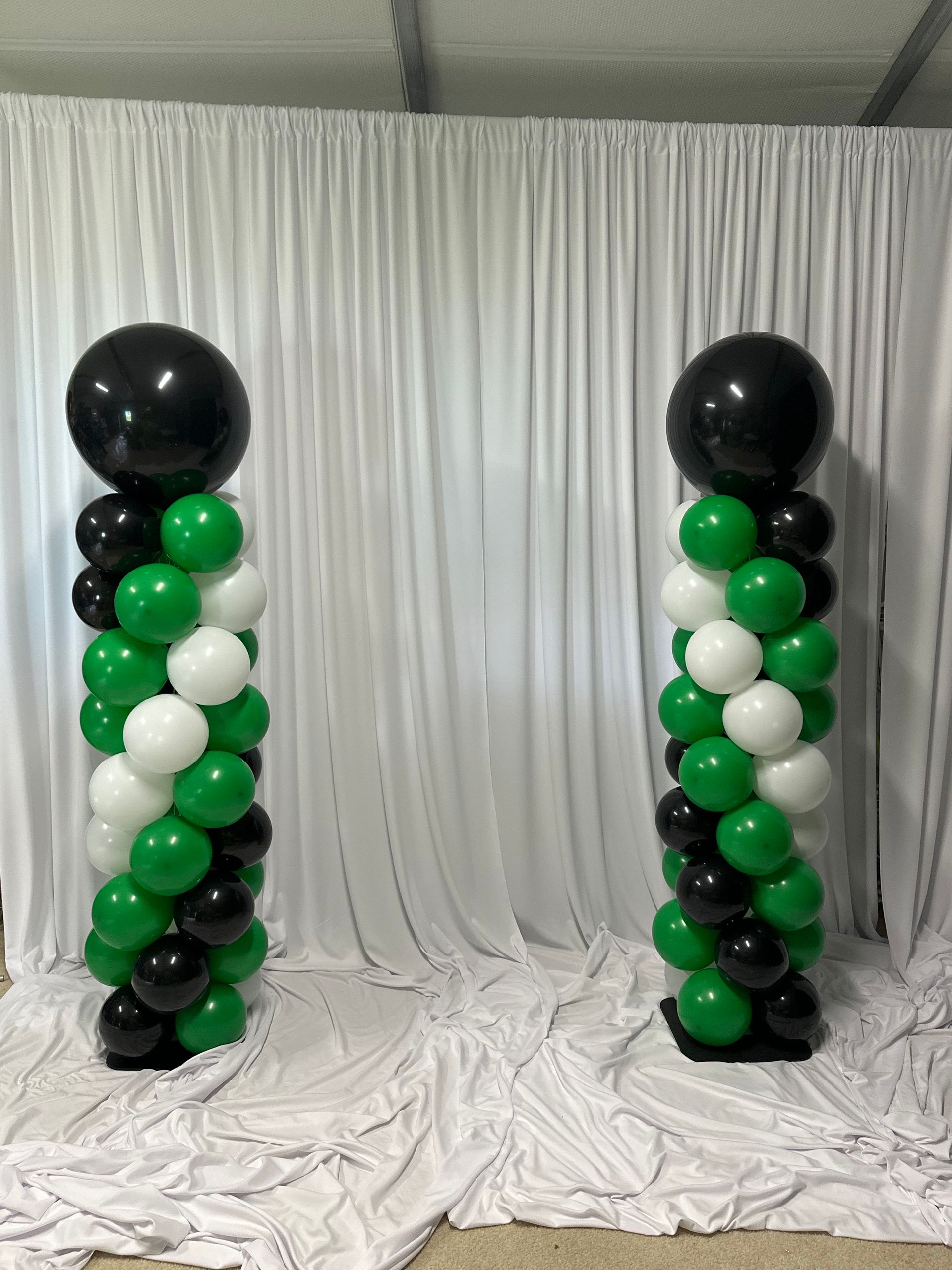 Two columns made of green , white and black balloons are sitting in front of a white curtain.