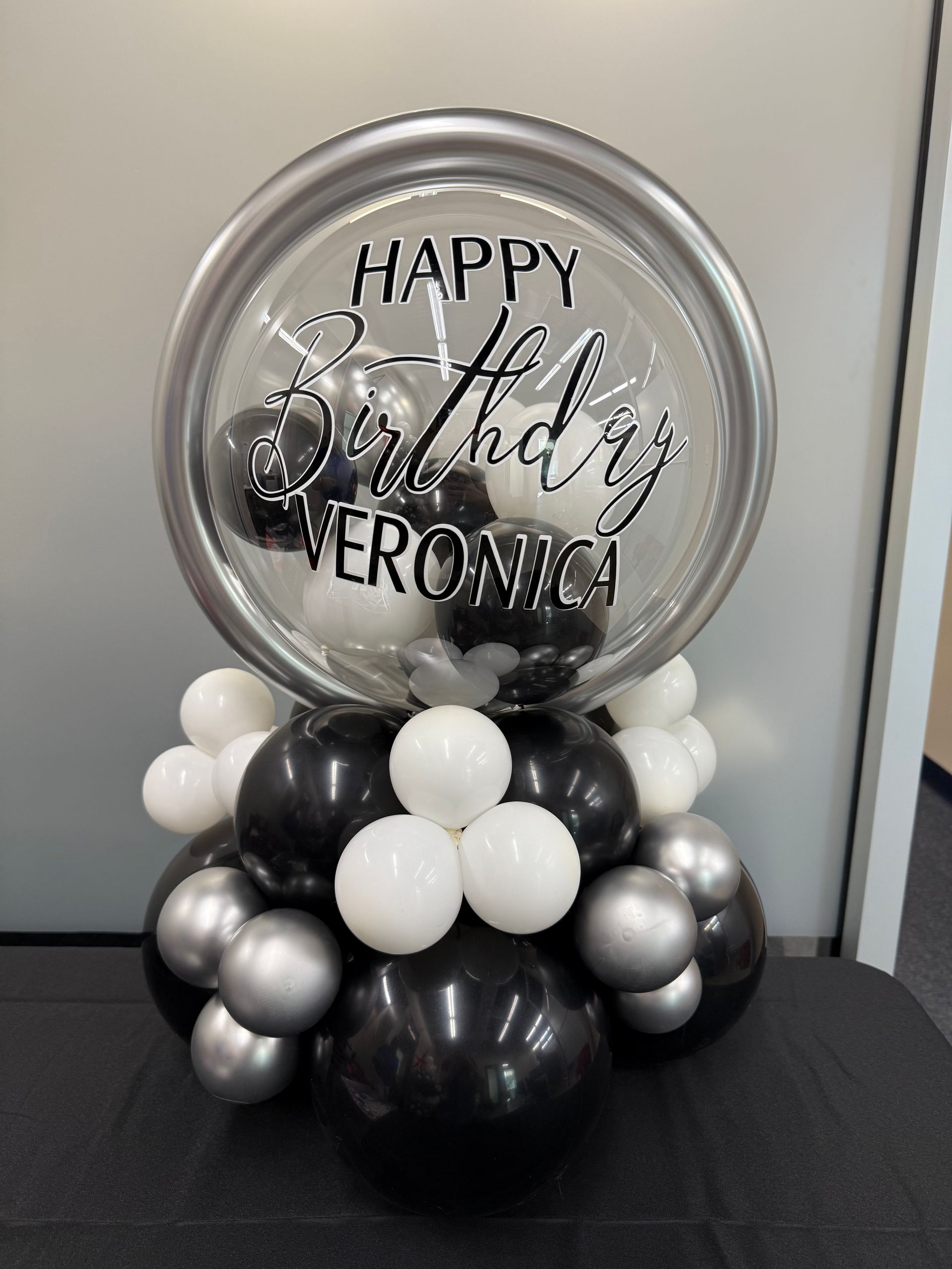 A happy birthday balloon is surrounded by black and white balloons.