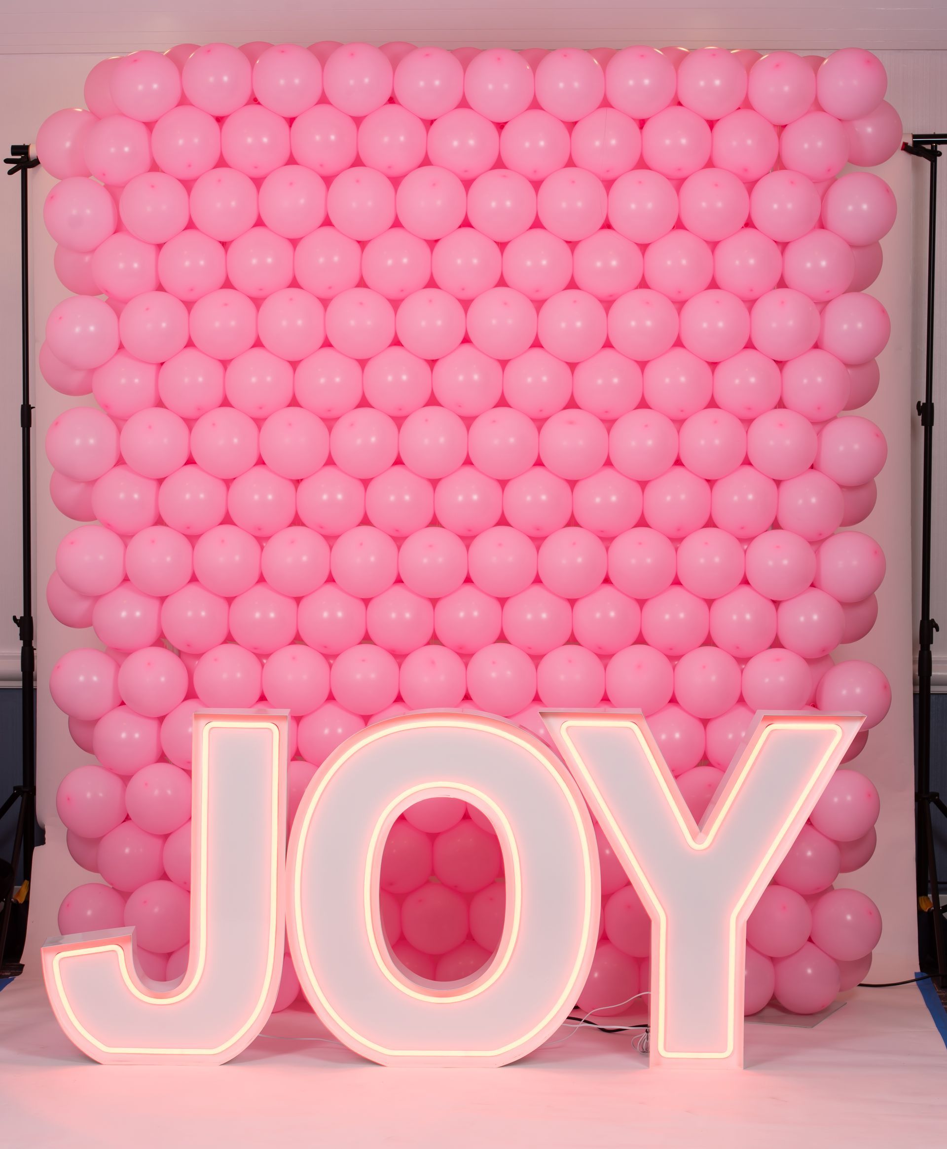 A wall of pink balloons with the word joy in white letters