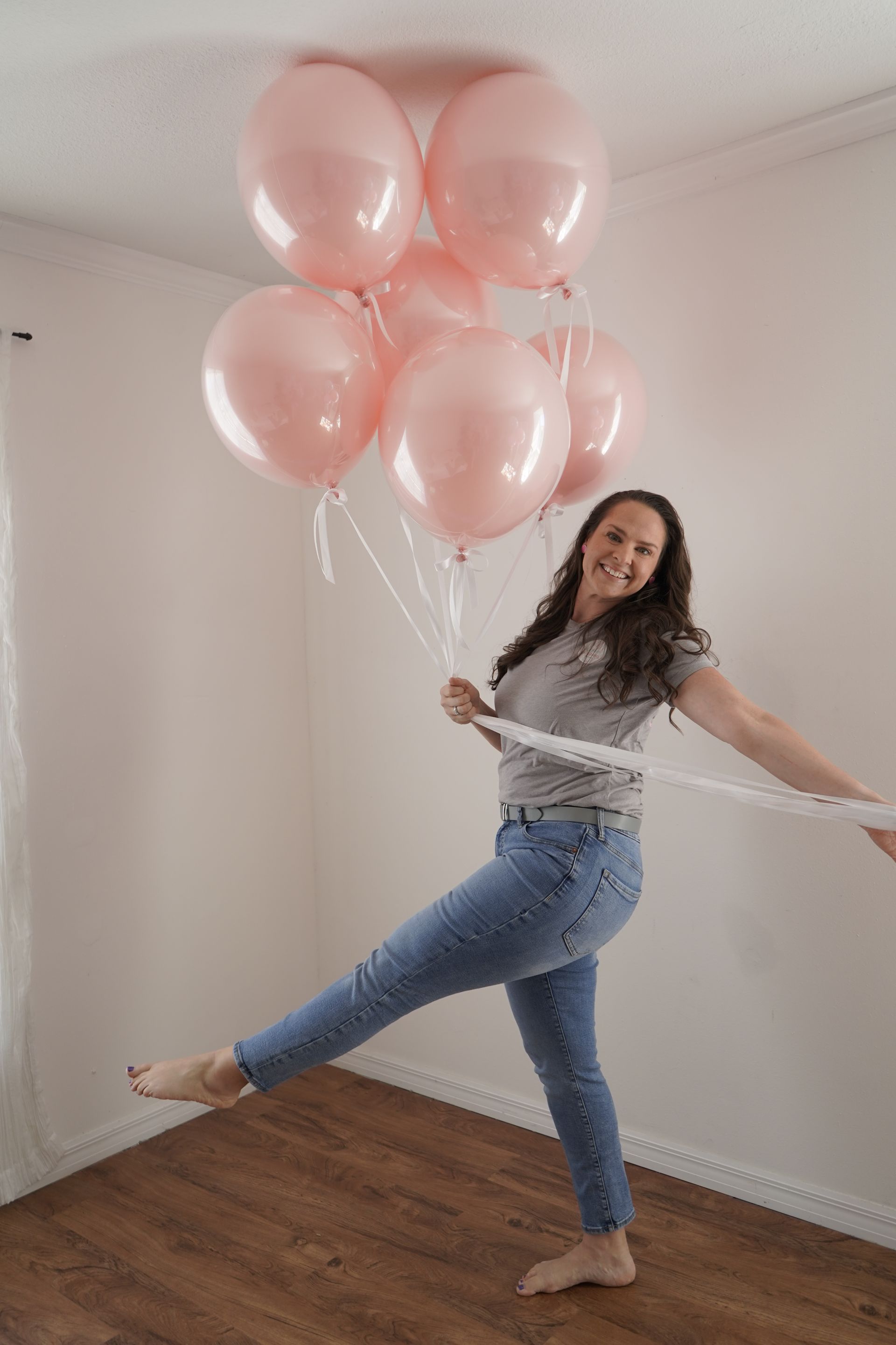 A woman is holding a bunch of pink balloons in a room.