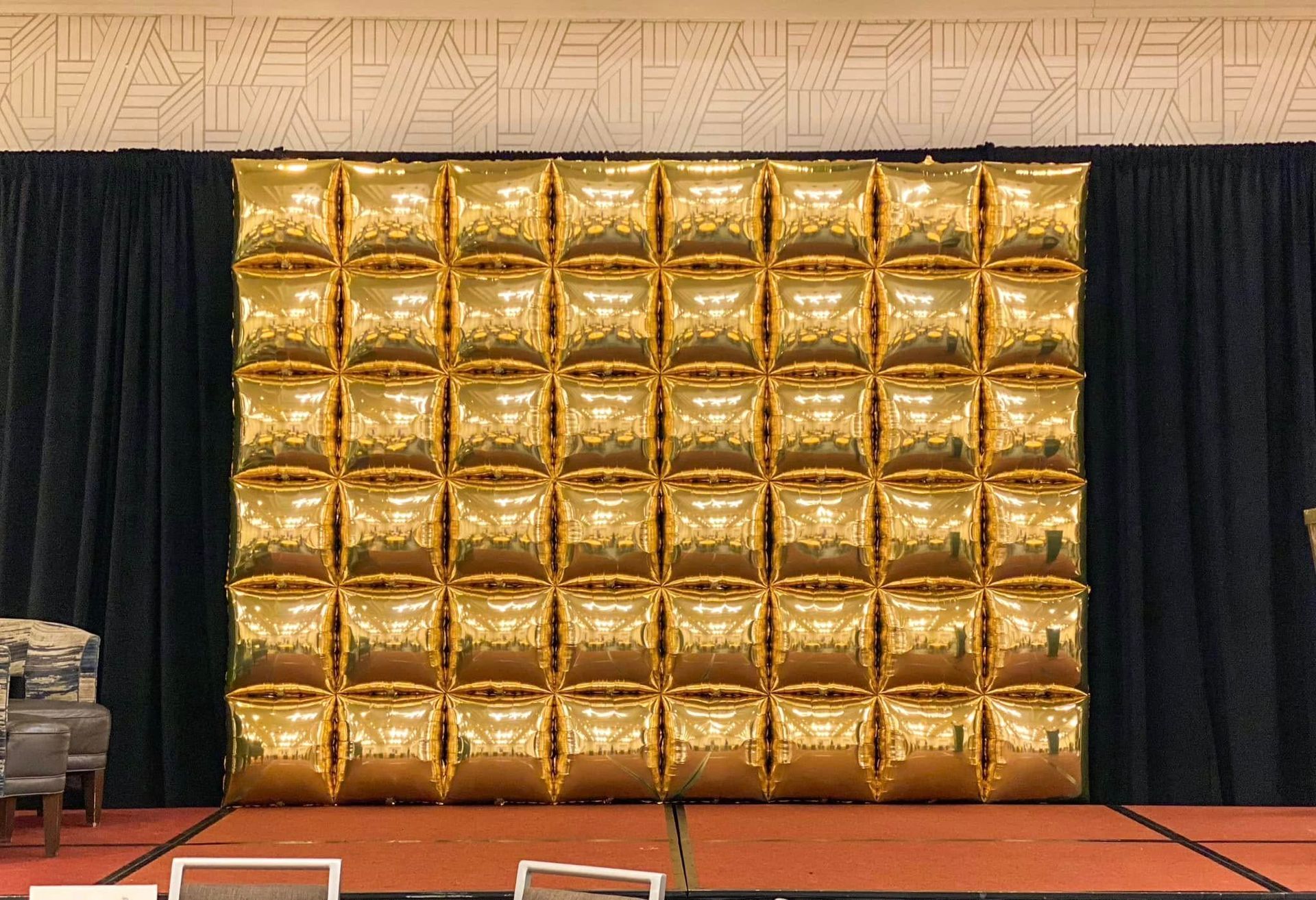 A large wall of gold balloons is behind a black curtain.