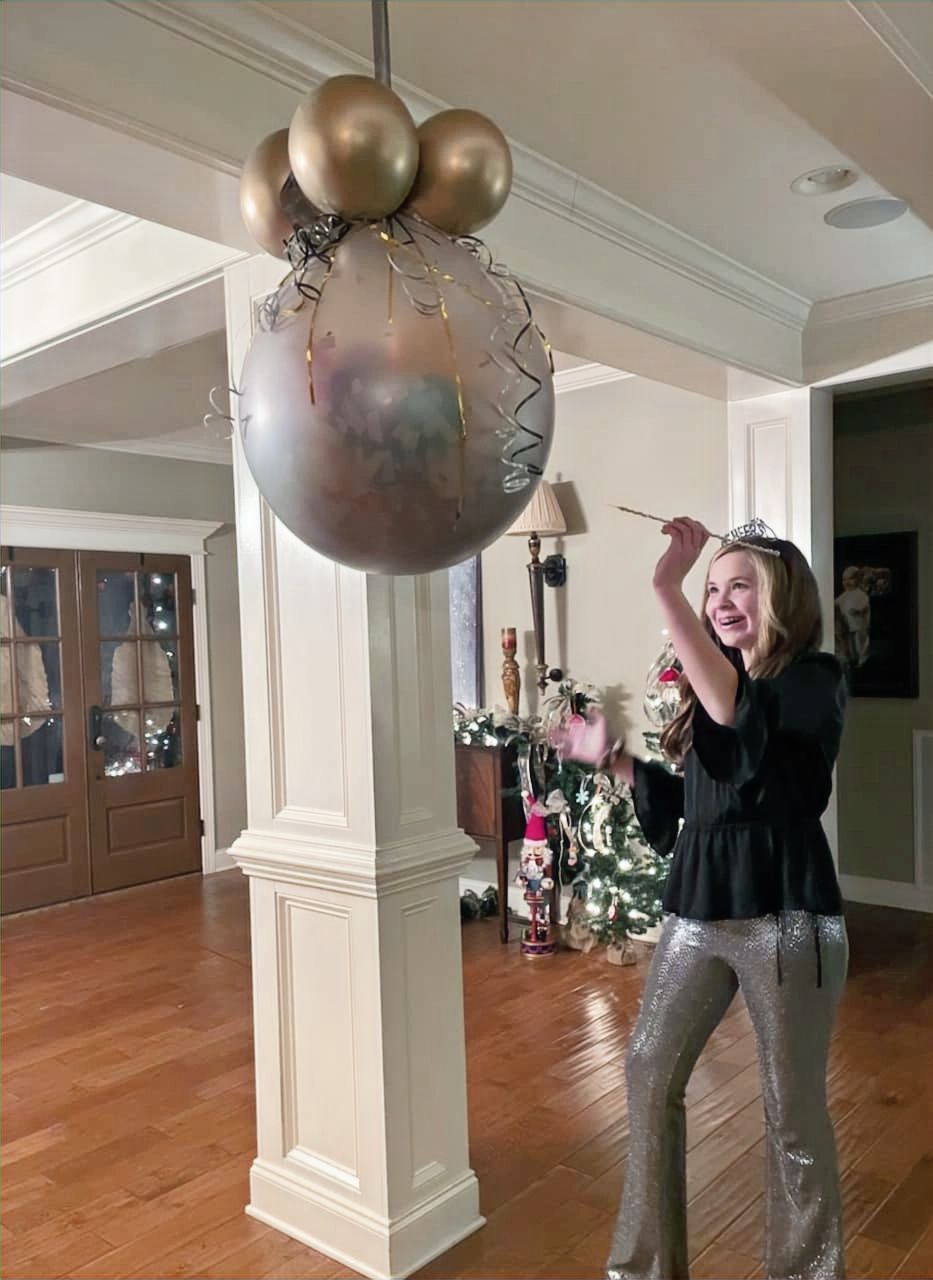 A girl is standing in front of a large balloon in a living room.