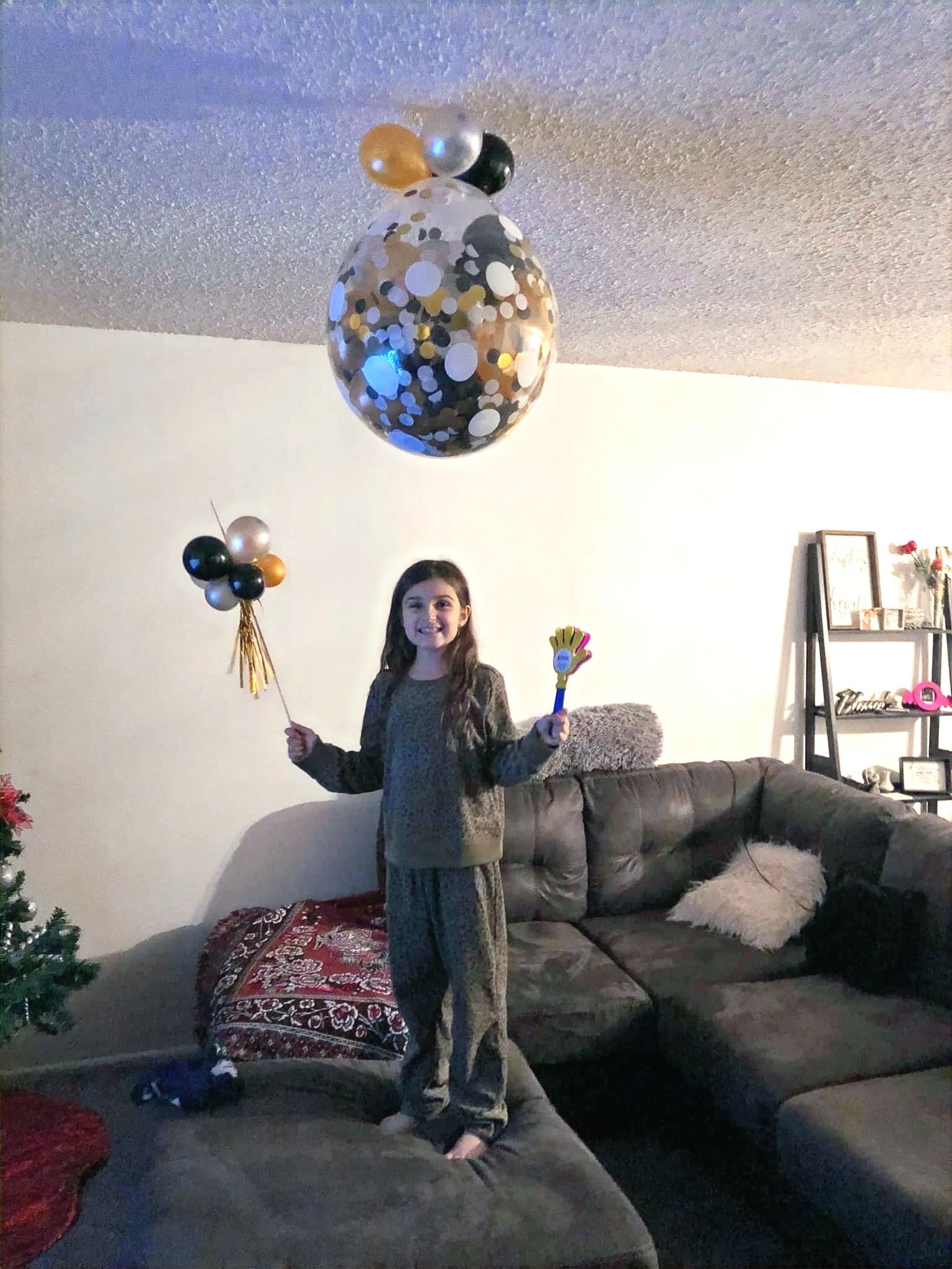 A little girl is standing in a living room holding balloons.