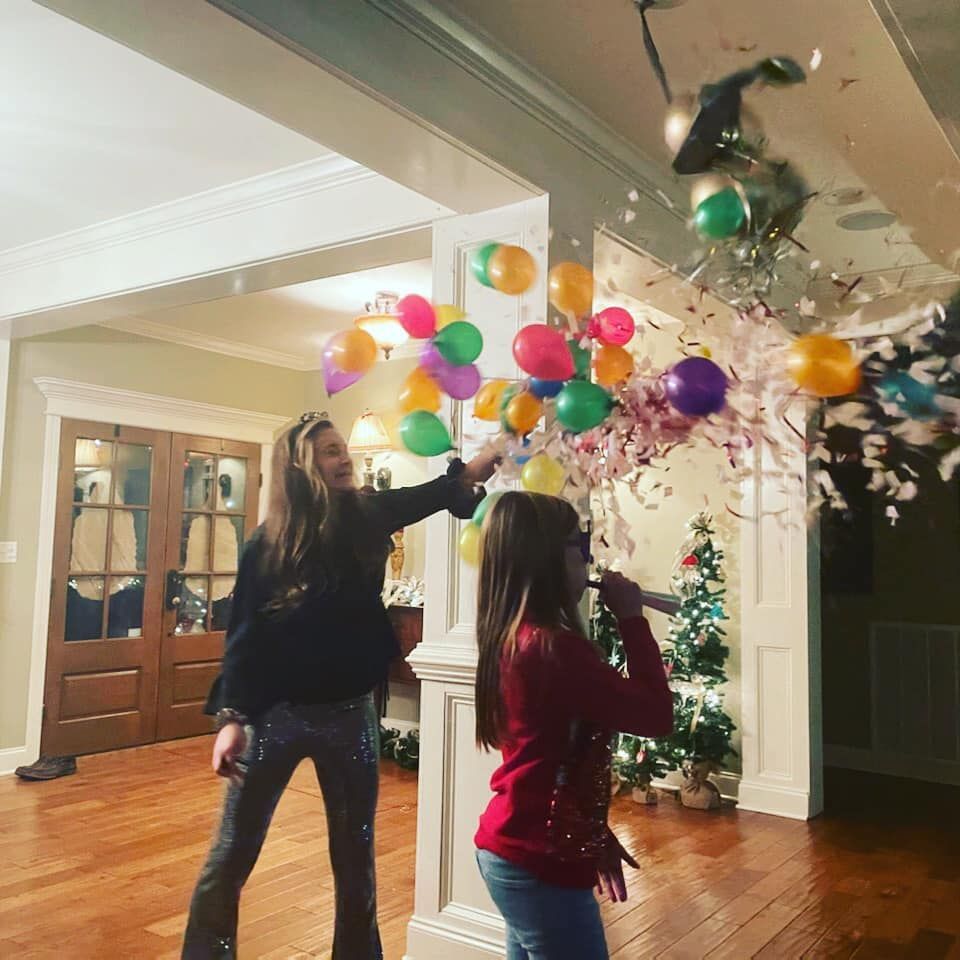 Two girls are playing with balloons and confetti in a living room
