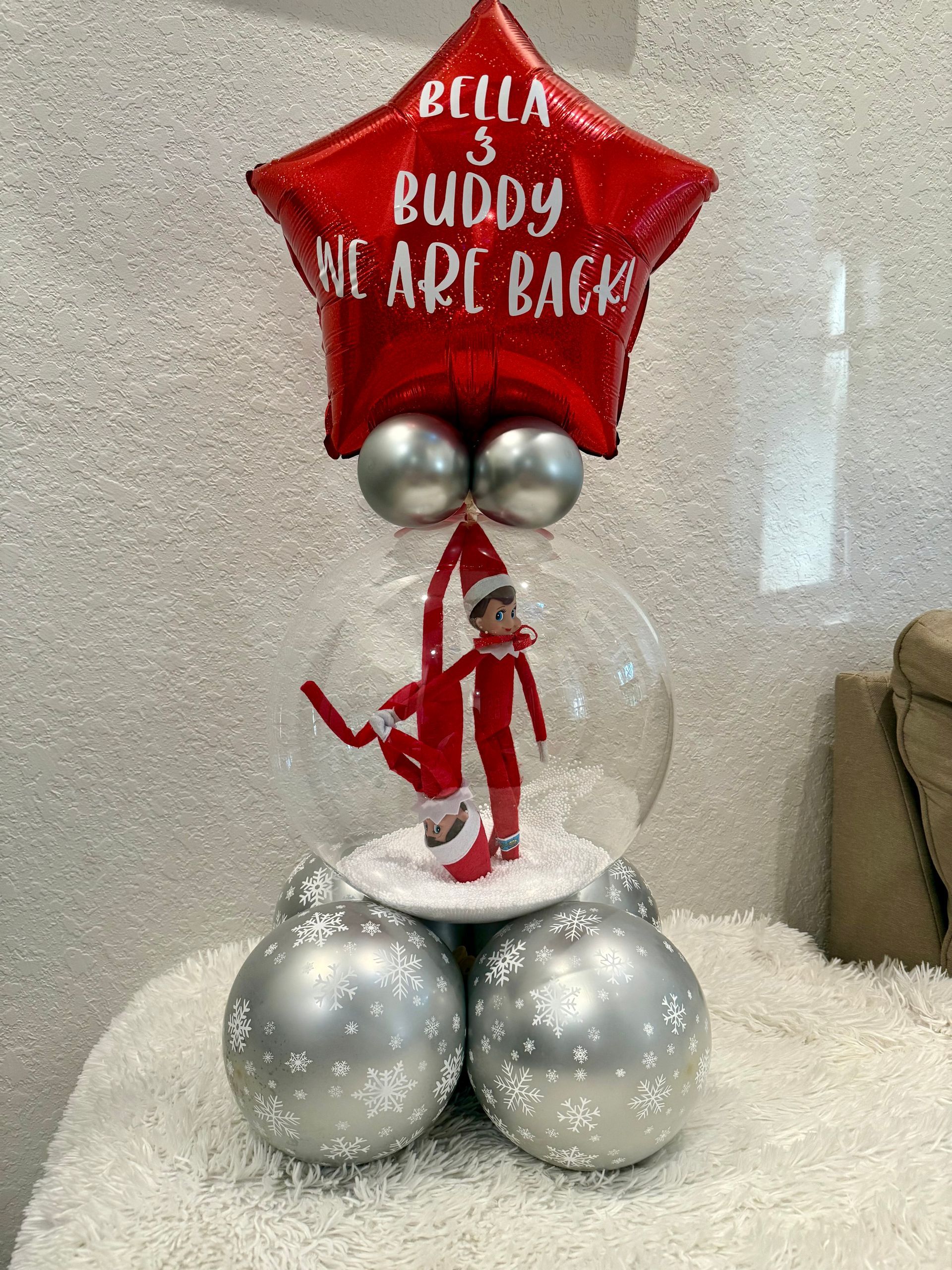 The elf on the shelf is in a snow globe with balloons.
