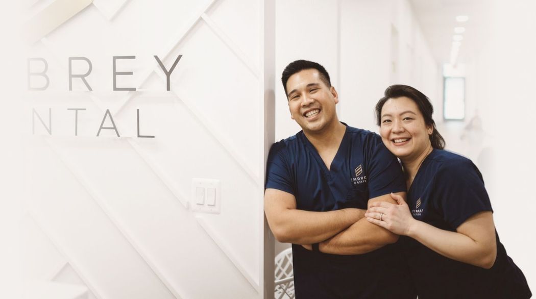 Two smiling people in dark uniforms standing by a BREX Dental sign