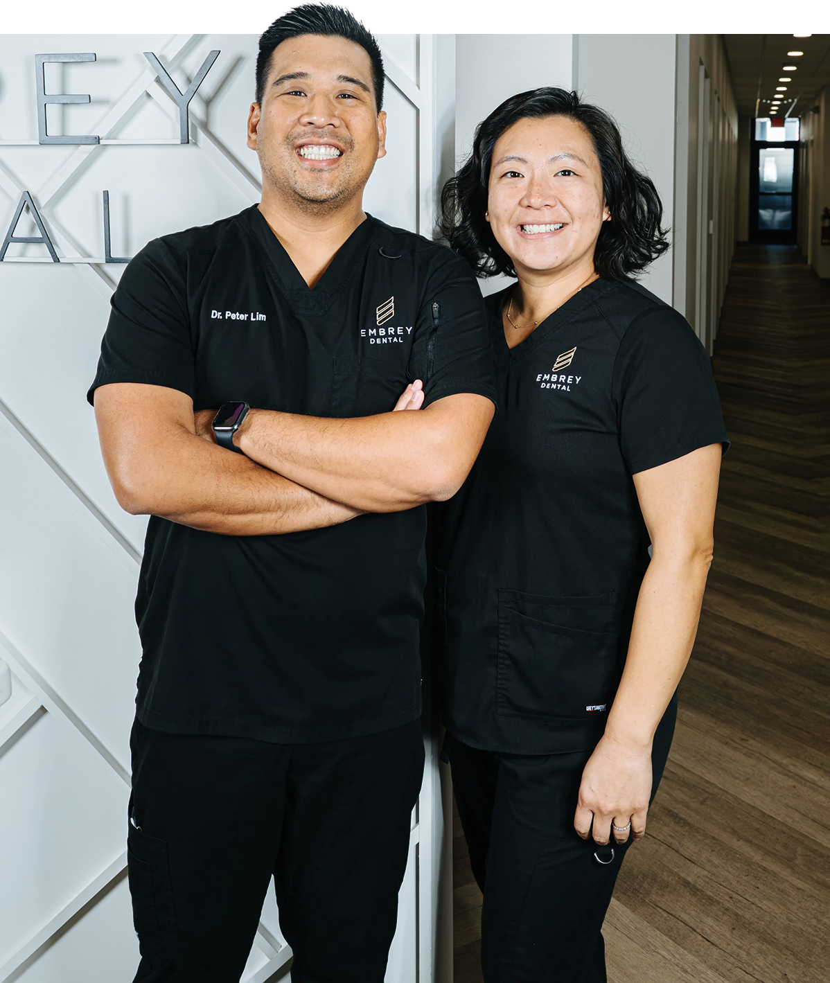Dr Lim and Rose in black scrubs smiling near a white wall with text.