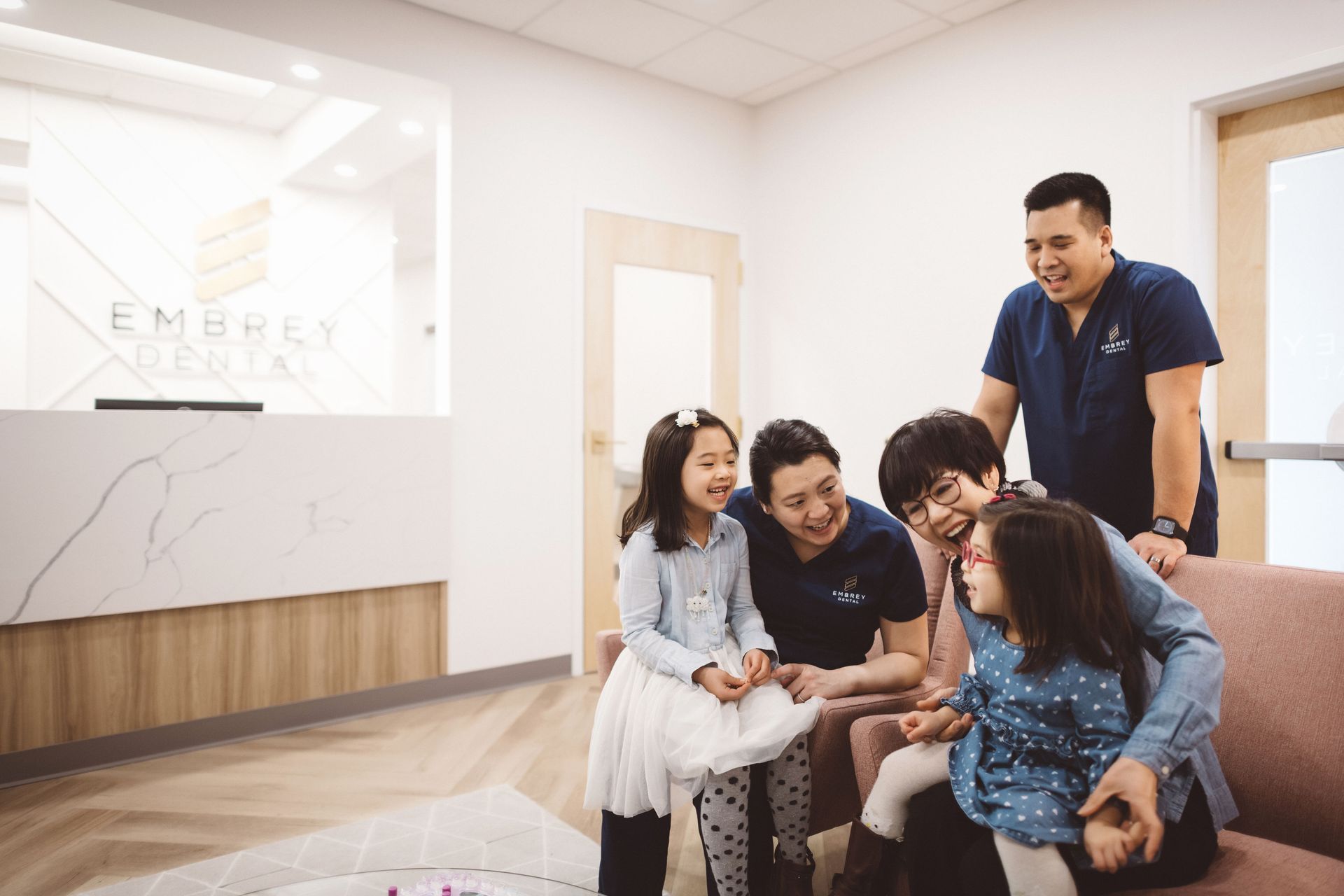 lim family sitting in the waiting room area smiling and happy together at Embrey Family Dental