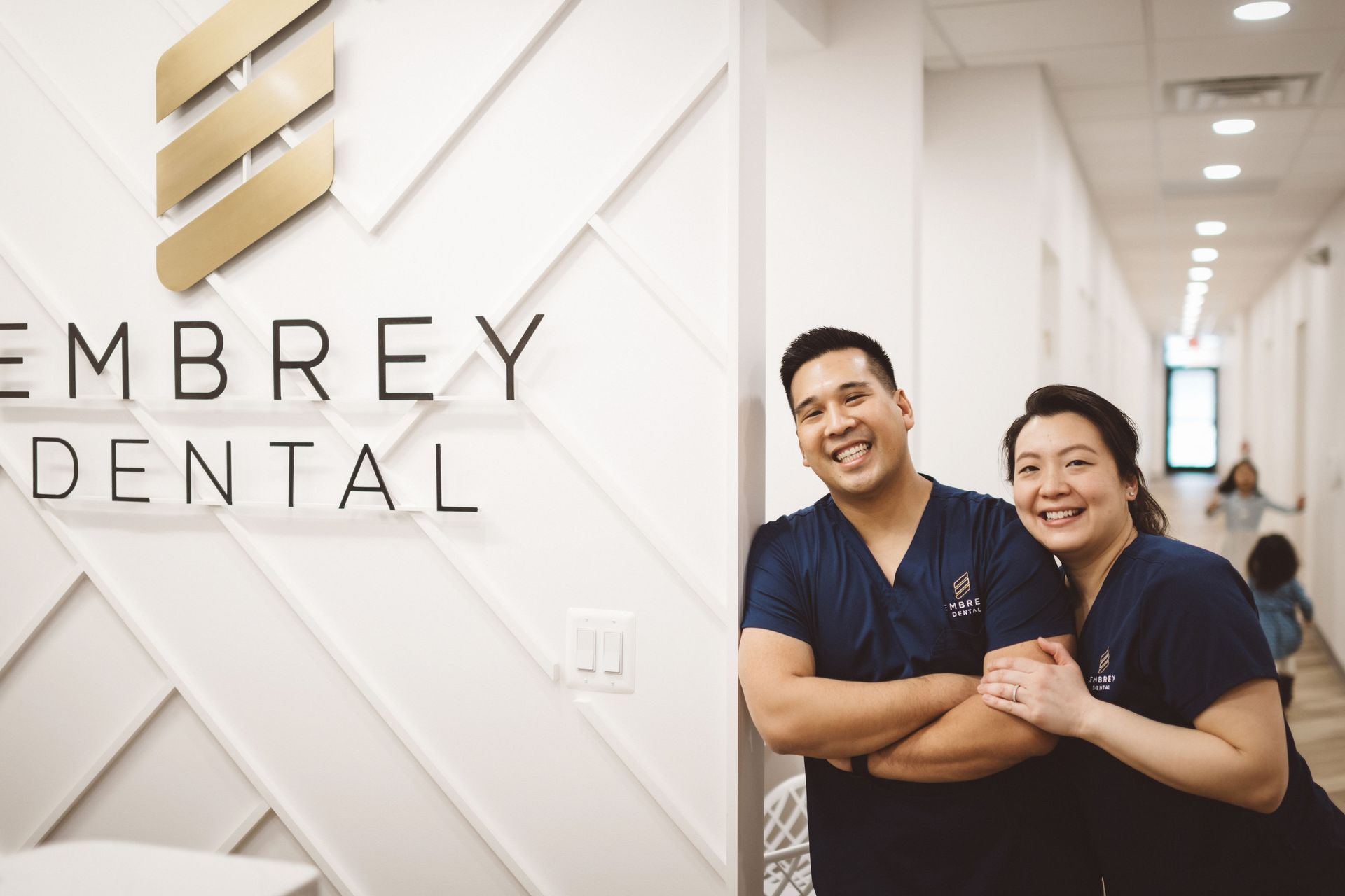 Dr lim and office manager Rose Lim standing by the front office logo wall smiling