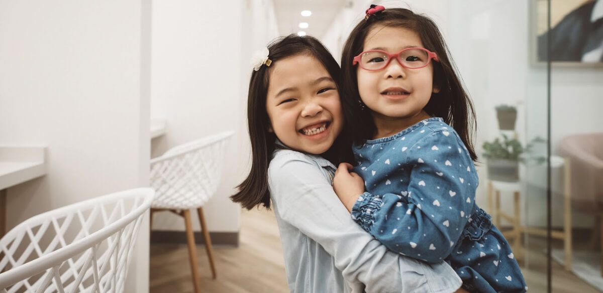 Smiling child hugging a woman indoors, with a white chair and glass door in the background