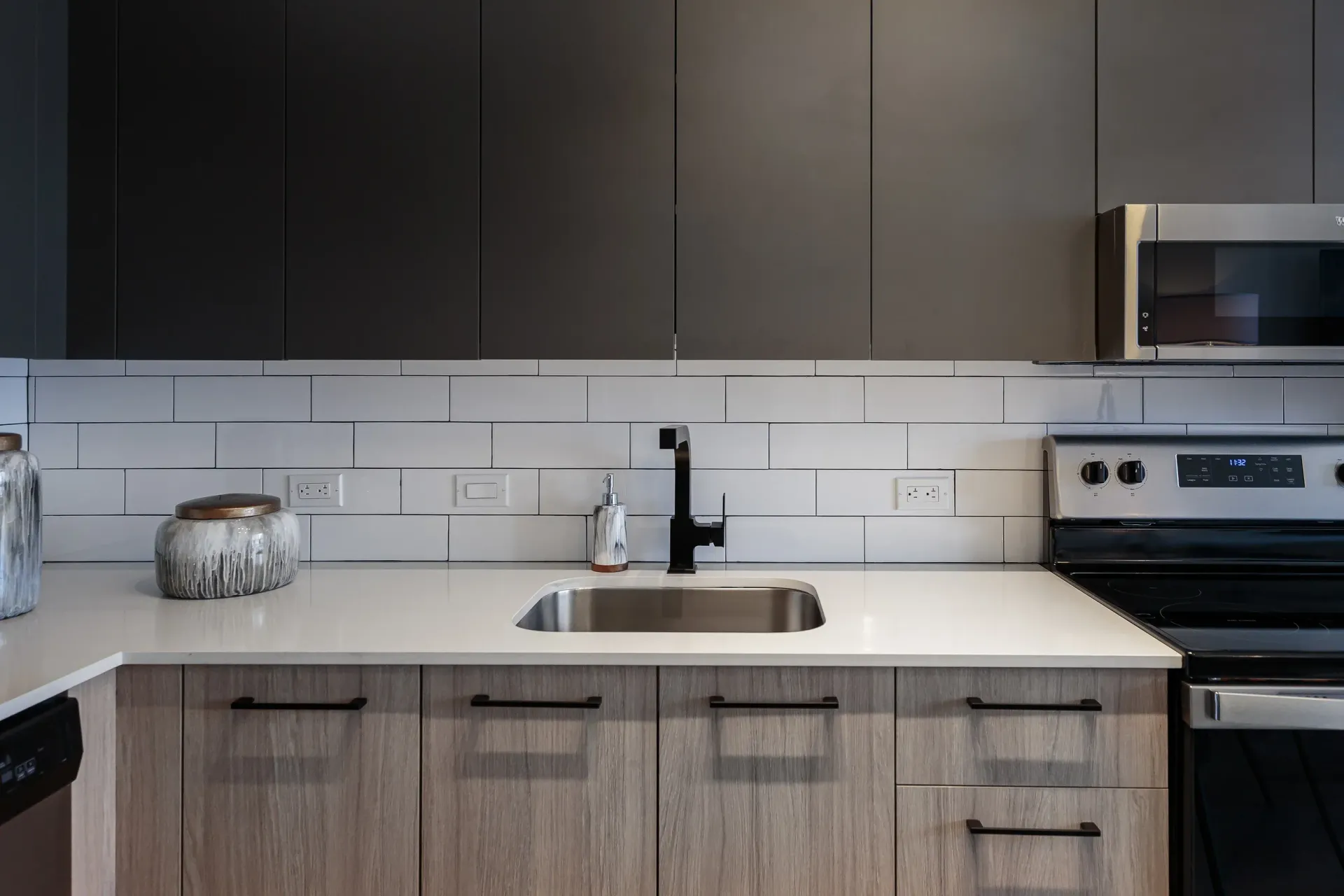 Modern kitchen with dark upper cabinets, light countertop, subway tile backsplash, and stainless steel sink.
