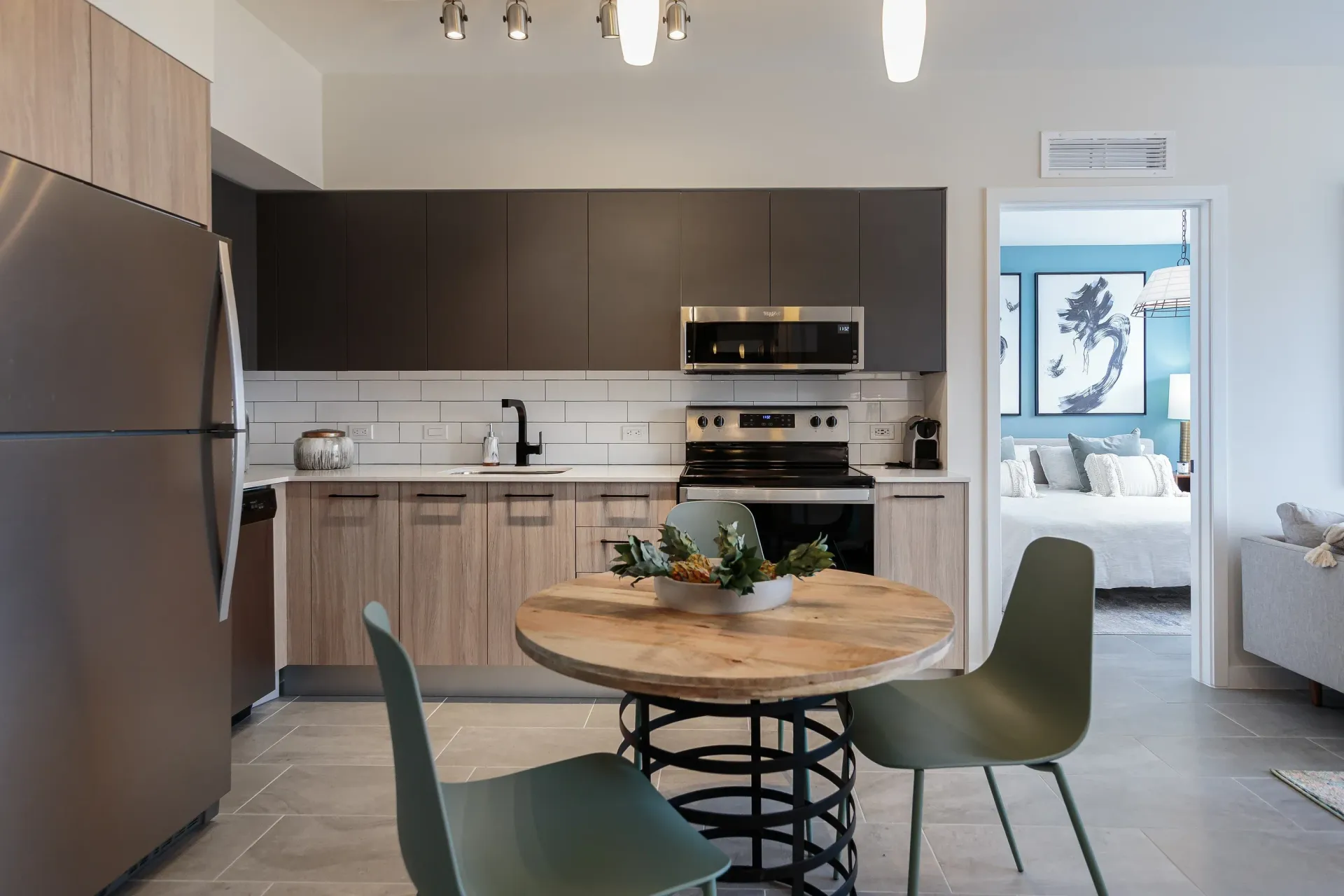Modern kitchen with stainless steel appliances, dark upper cabinets, and a round wooden dining table.