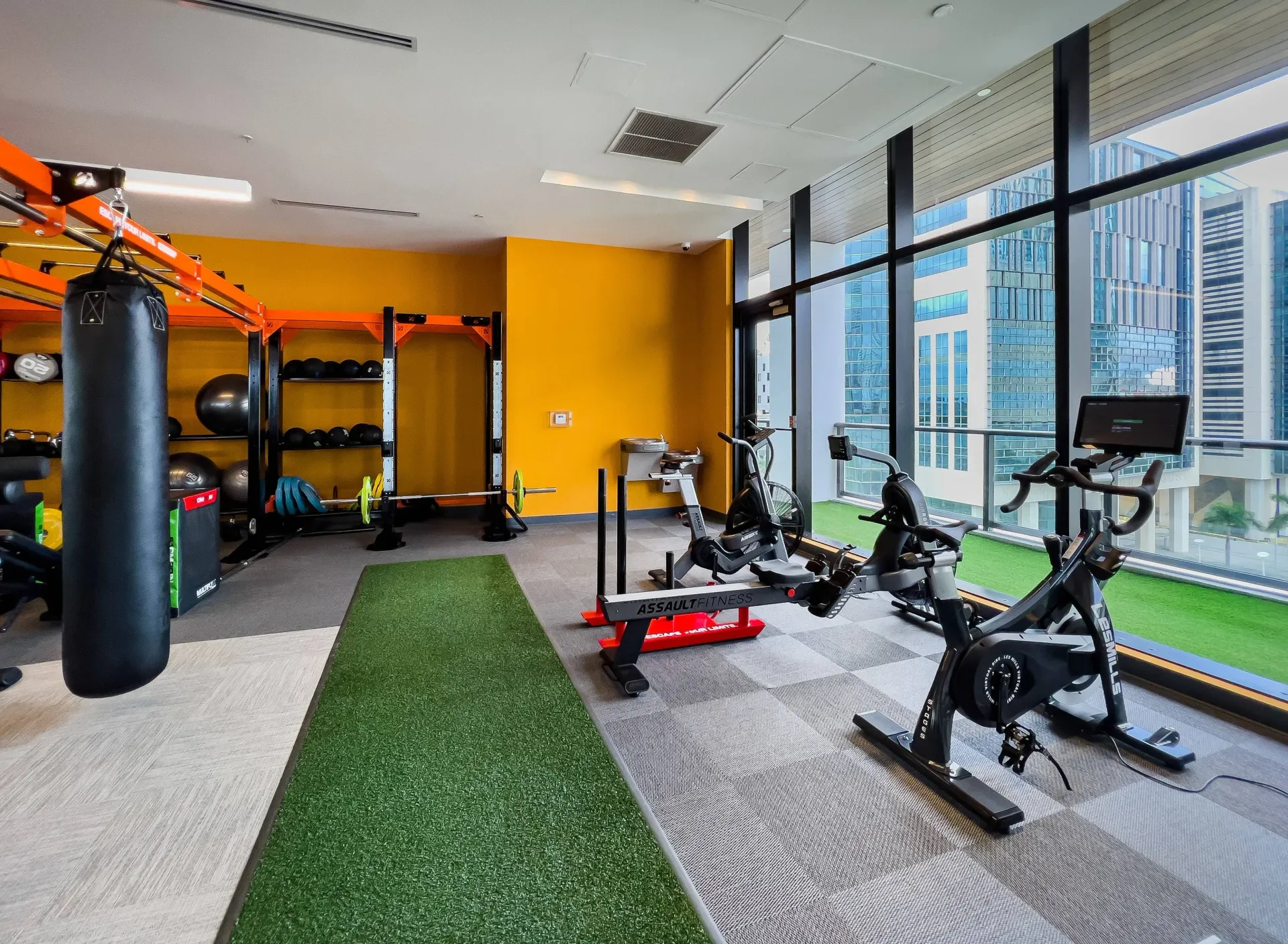 Fitness center with cardio machines, a weight rack, and a punching bag by large windows.