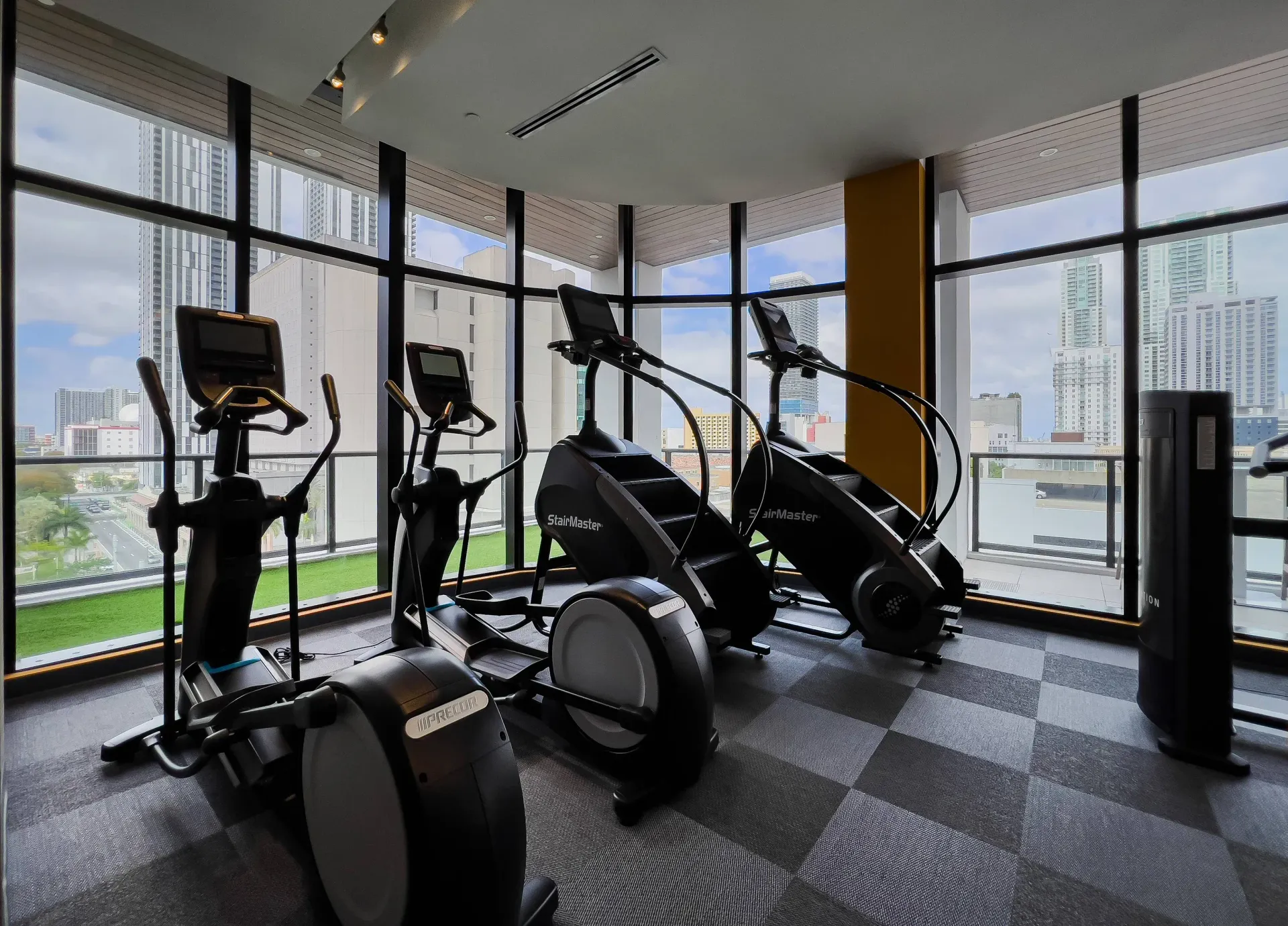 Indoor fitness center with cardio machines and large glass windows overlooking the city skyline.