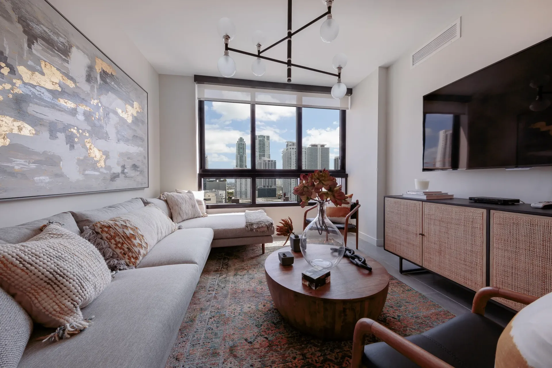 Contemporary living room with a gray sectional, round coffee table, and city skyline view.