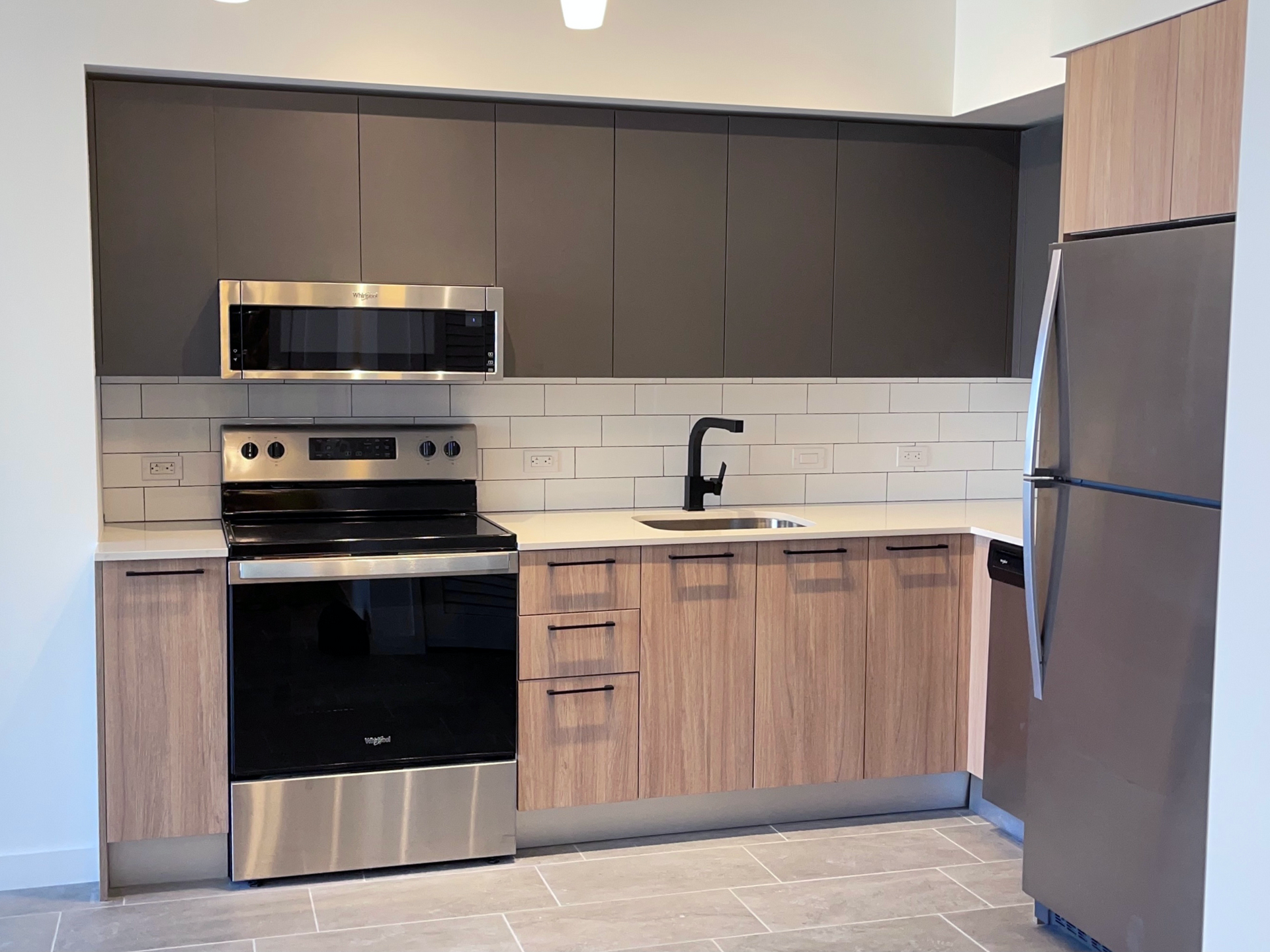 Modern kitchen with stainless-steel appliances, dark upper cabinets, wood-toned lowers, and a black faucet.