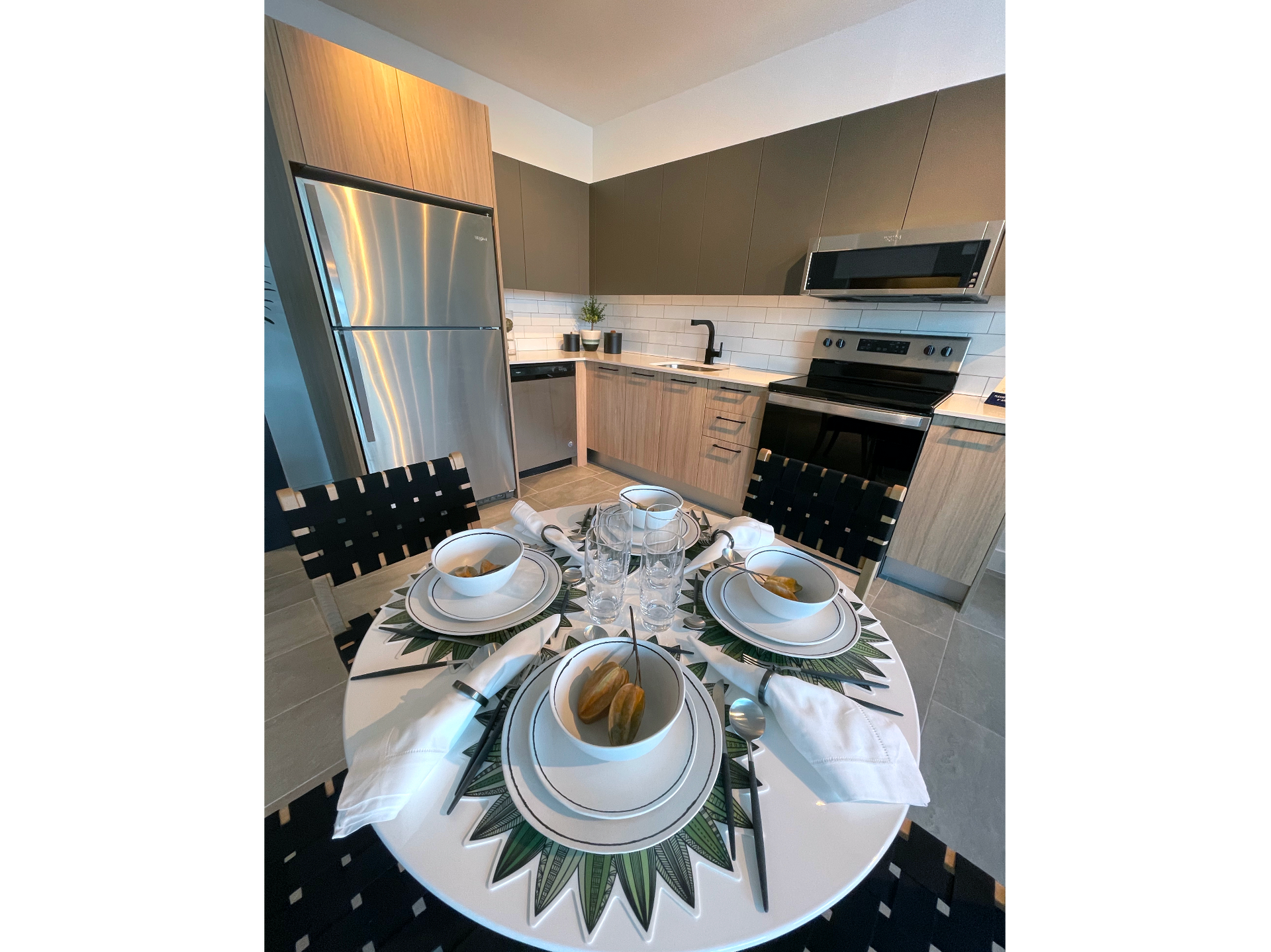 Modern apartment kitchen with stainless steel fridge, oven, microwave, and a round dining table set for four.