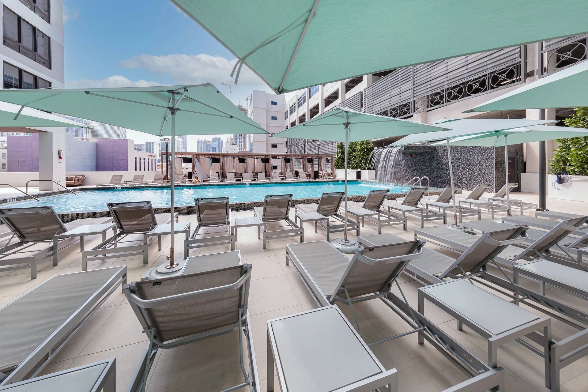 Poolside scene with lounge chairs, umbrellas, and a waterfall feature.