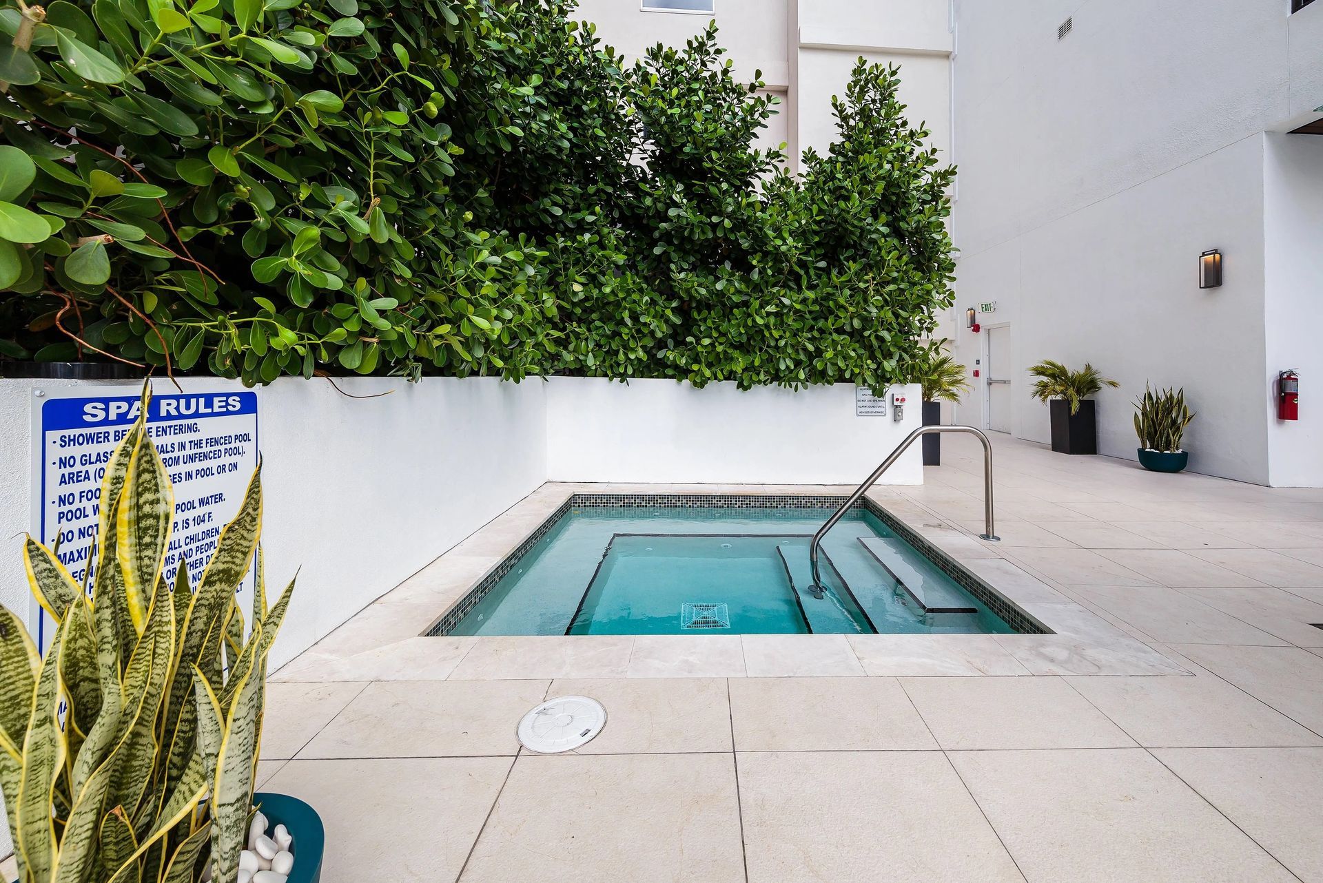 A small spa with steps and metal handrails, surrounded by greenery, on a patio at Grand Station in Miami, FL.