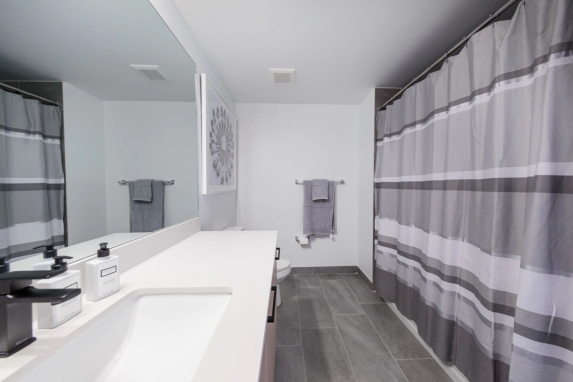 Bathroom with a sink and long countertop, shower curtain, and towel rack. Gray and white color scheme.
