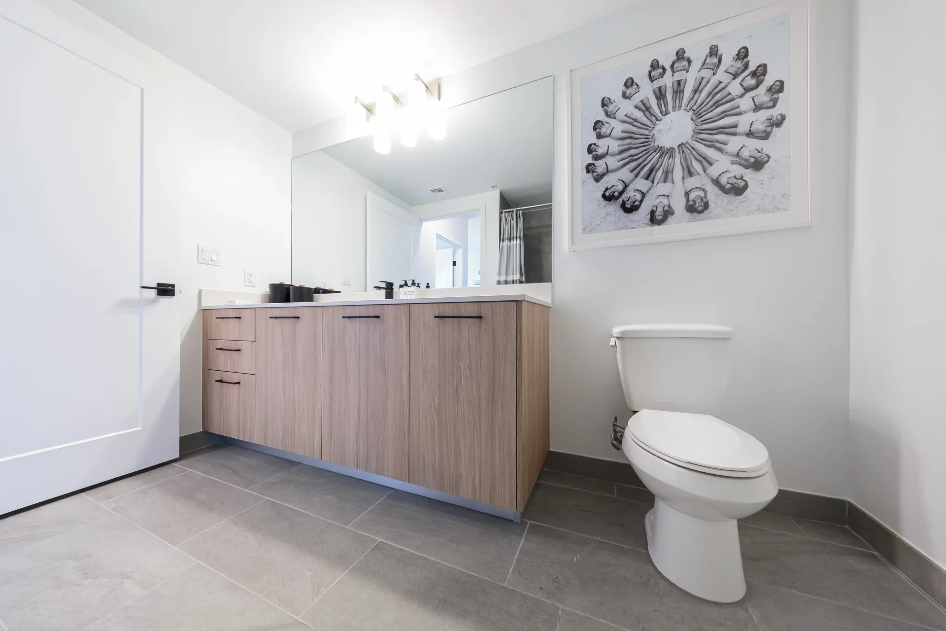 Modern bathroom with a wood-toned vanity, large mirror, and toilet.