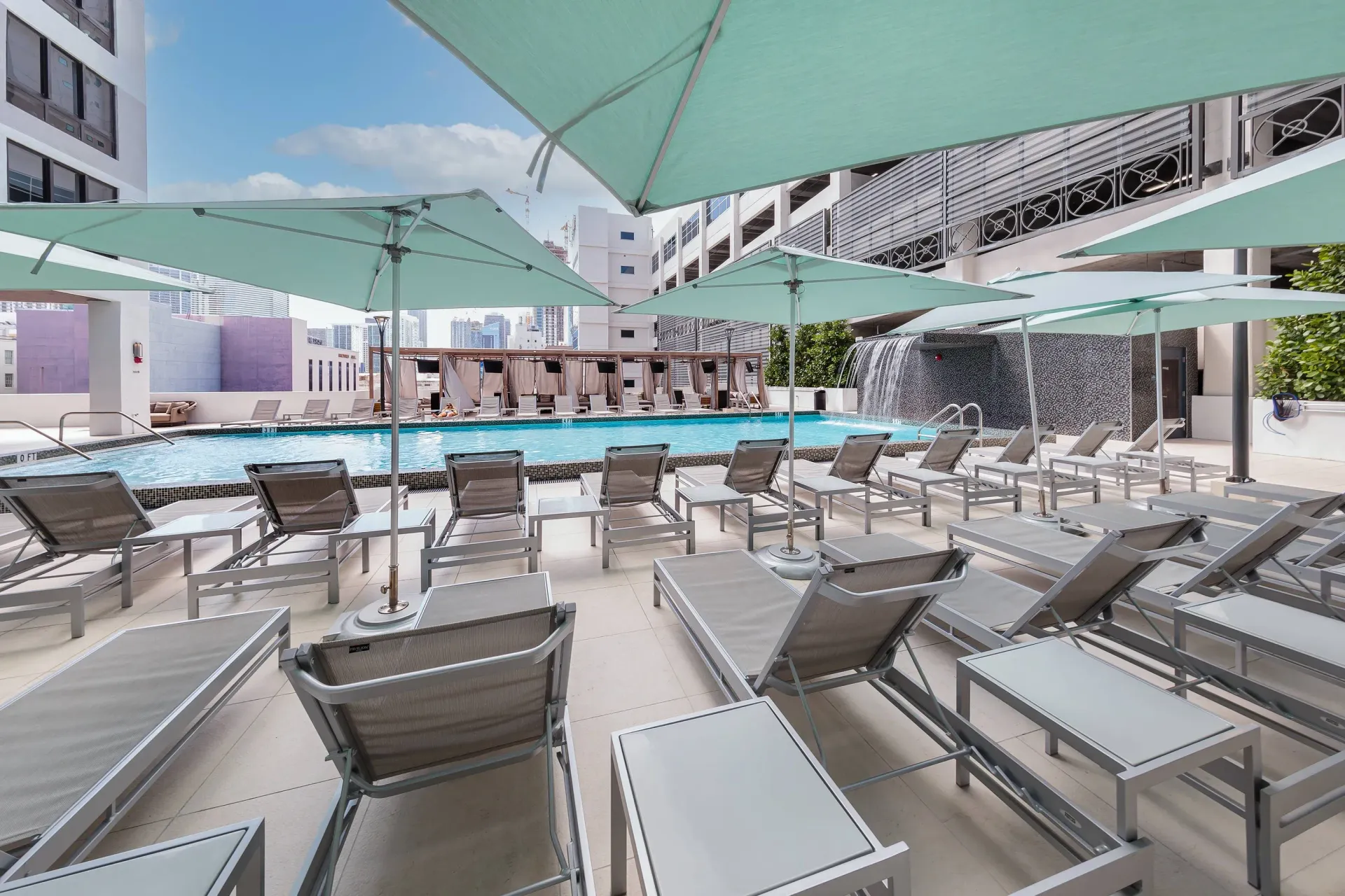 Rooftop pool area with lounge chairs and green shade sails.
