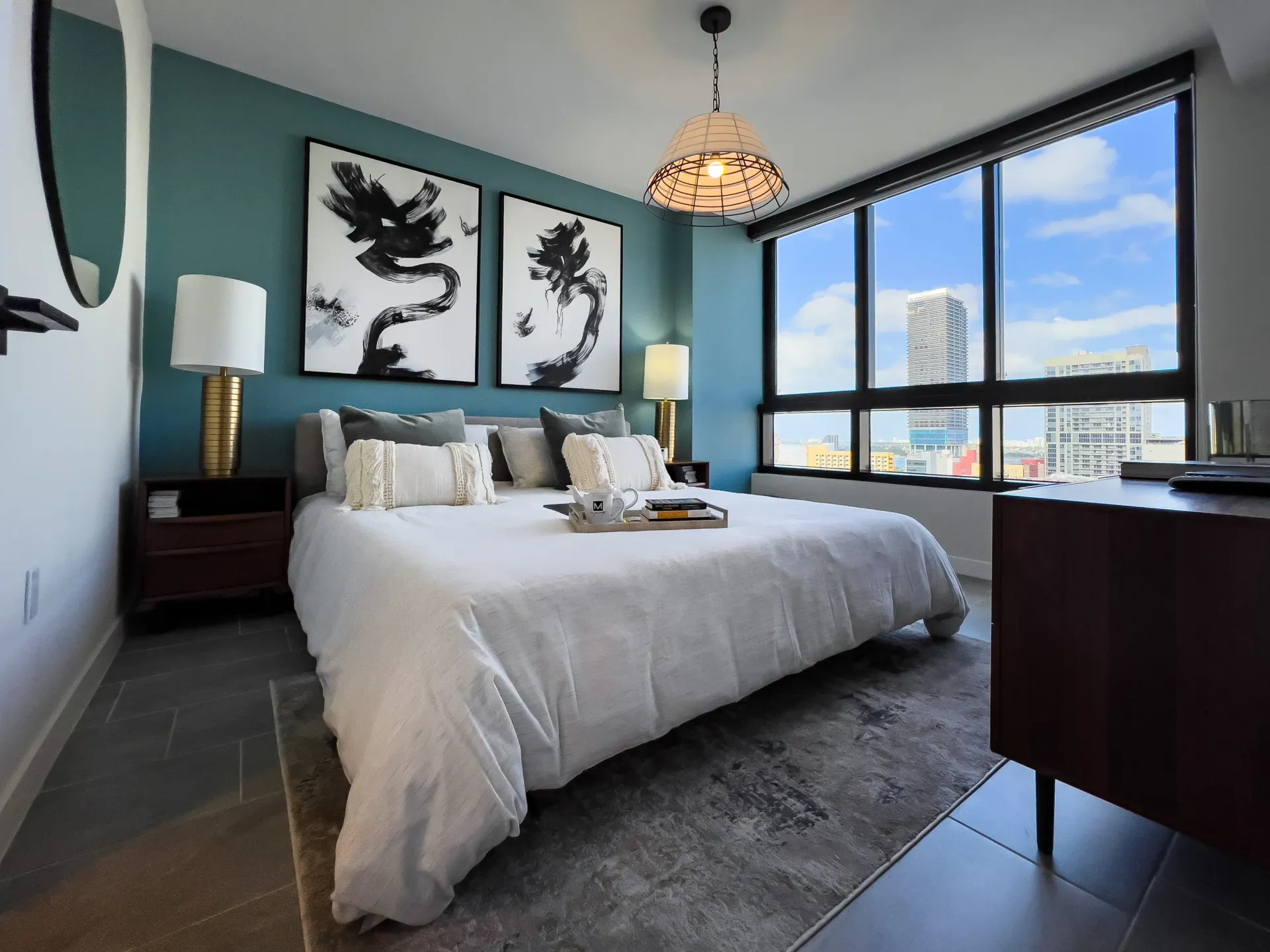 Bedroom in a high-rise city apartment with a teal accent wall and large window.