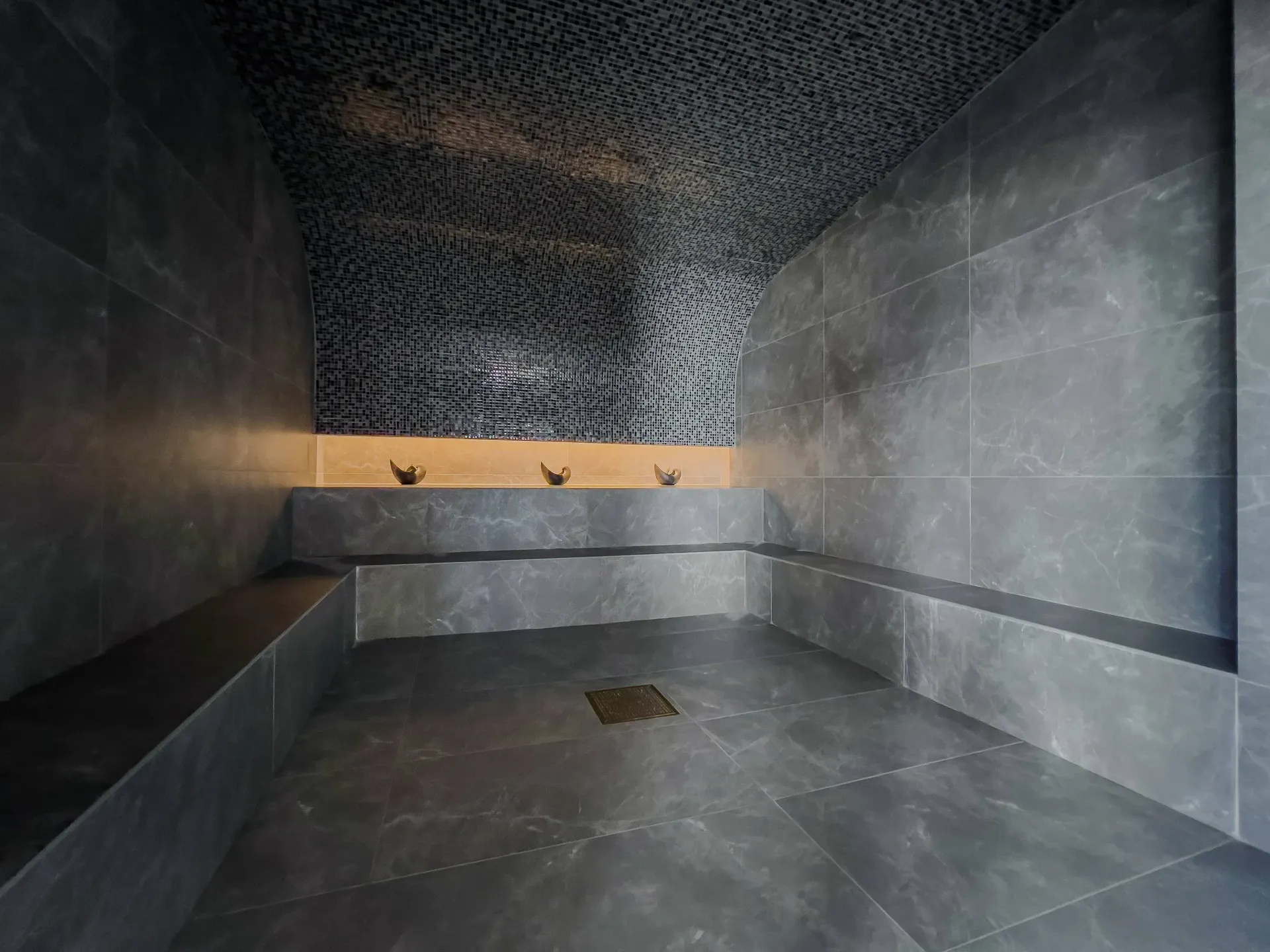 Dark tiled steam room with curved mosaic ceiling and built-in benches.