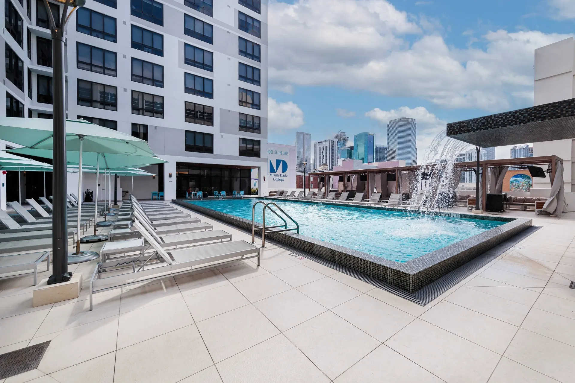 Rooftop pool deck with lounge chairs, umbrellas, and city skyline.