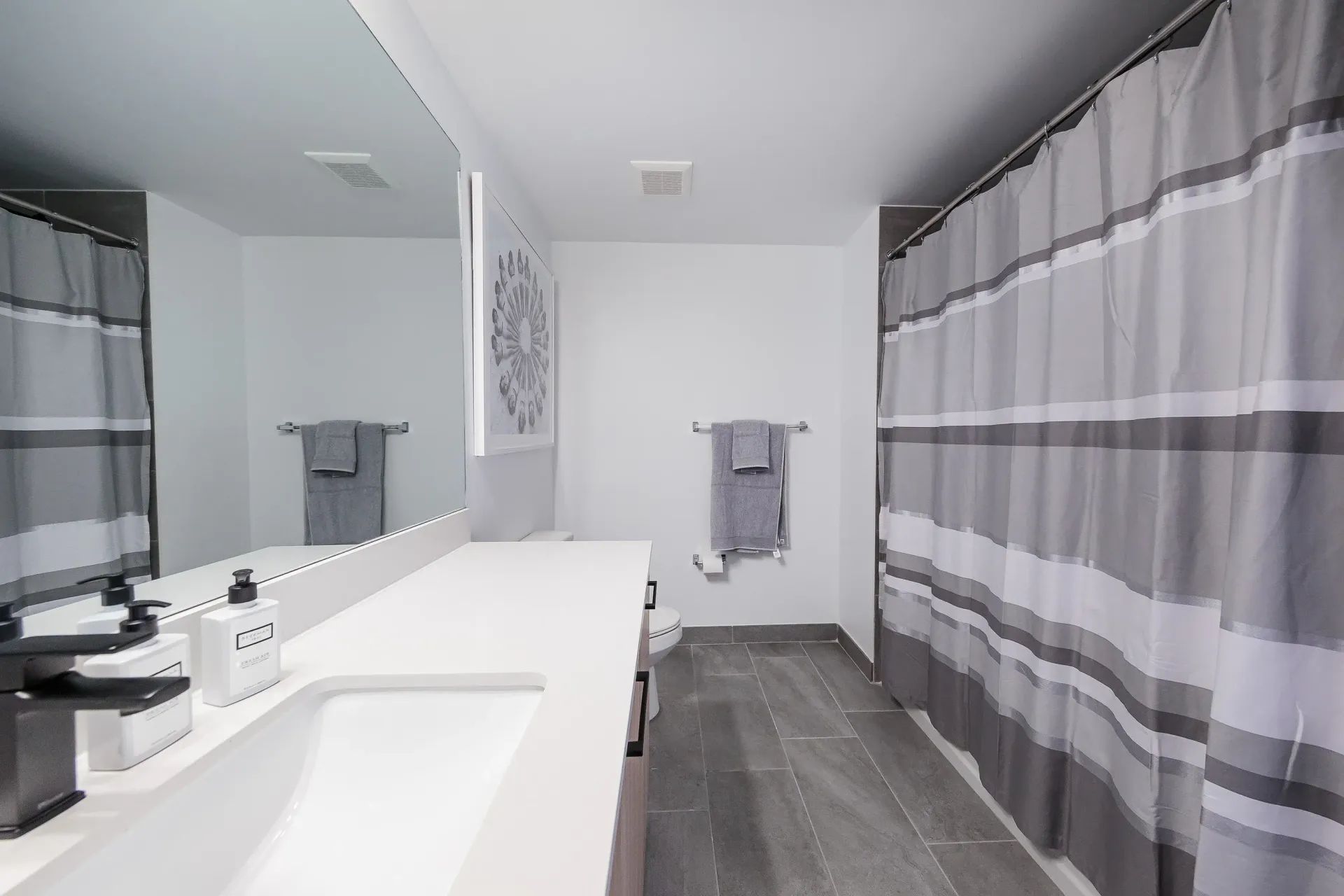 Modern apartment bathroom with a long white countertop, single sink, and gray striped shower curtain.