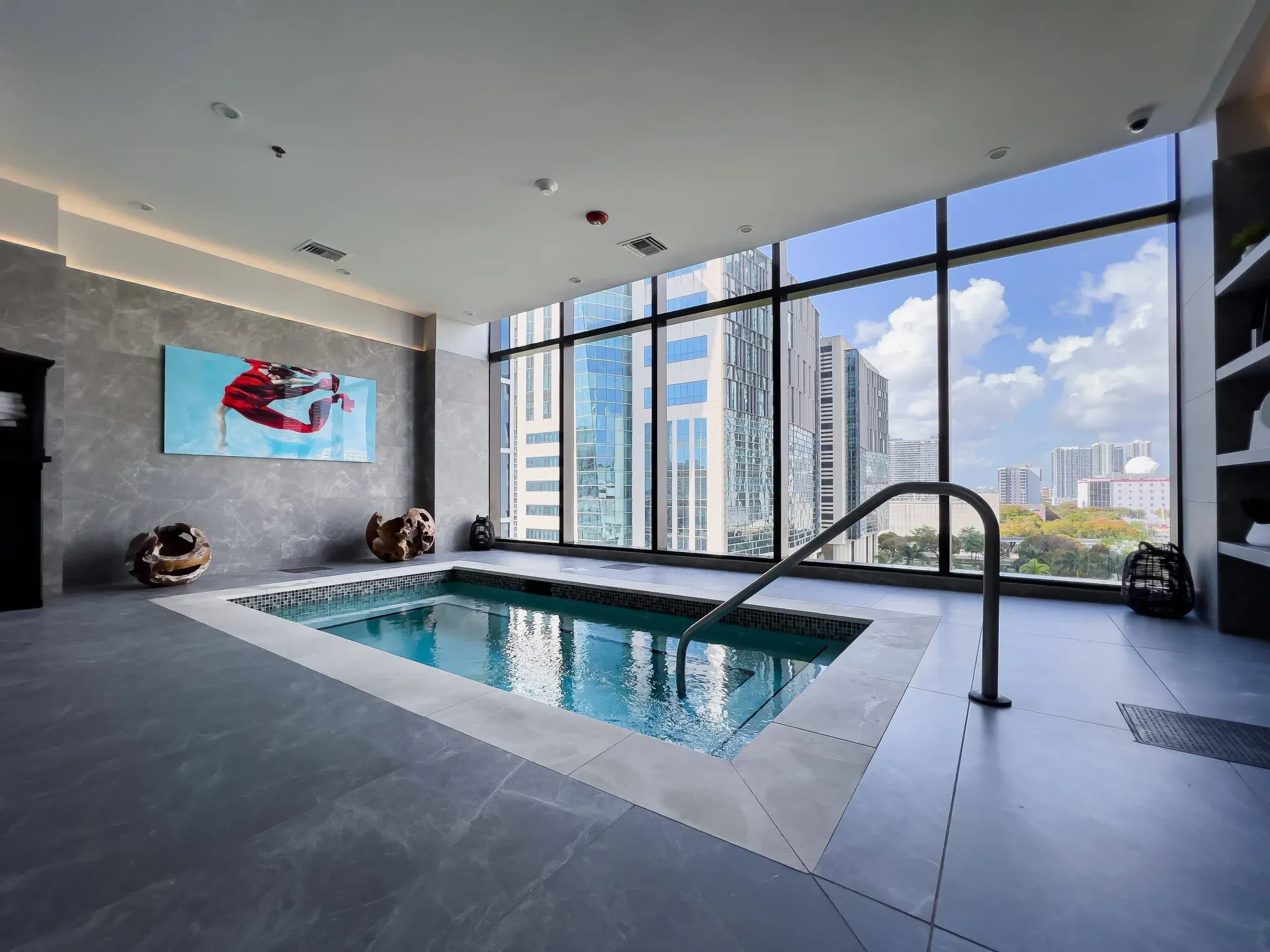 Indoor pool area in a high-rise building with large windows and city skyline view.