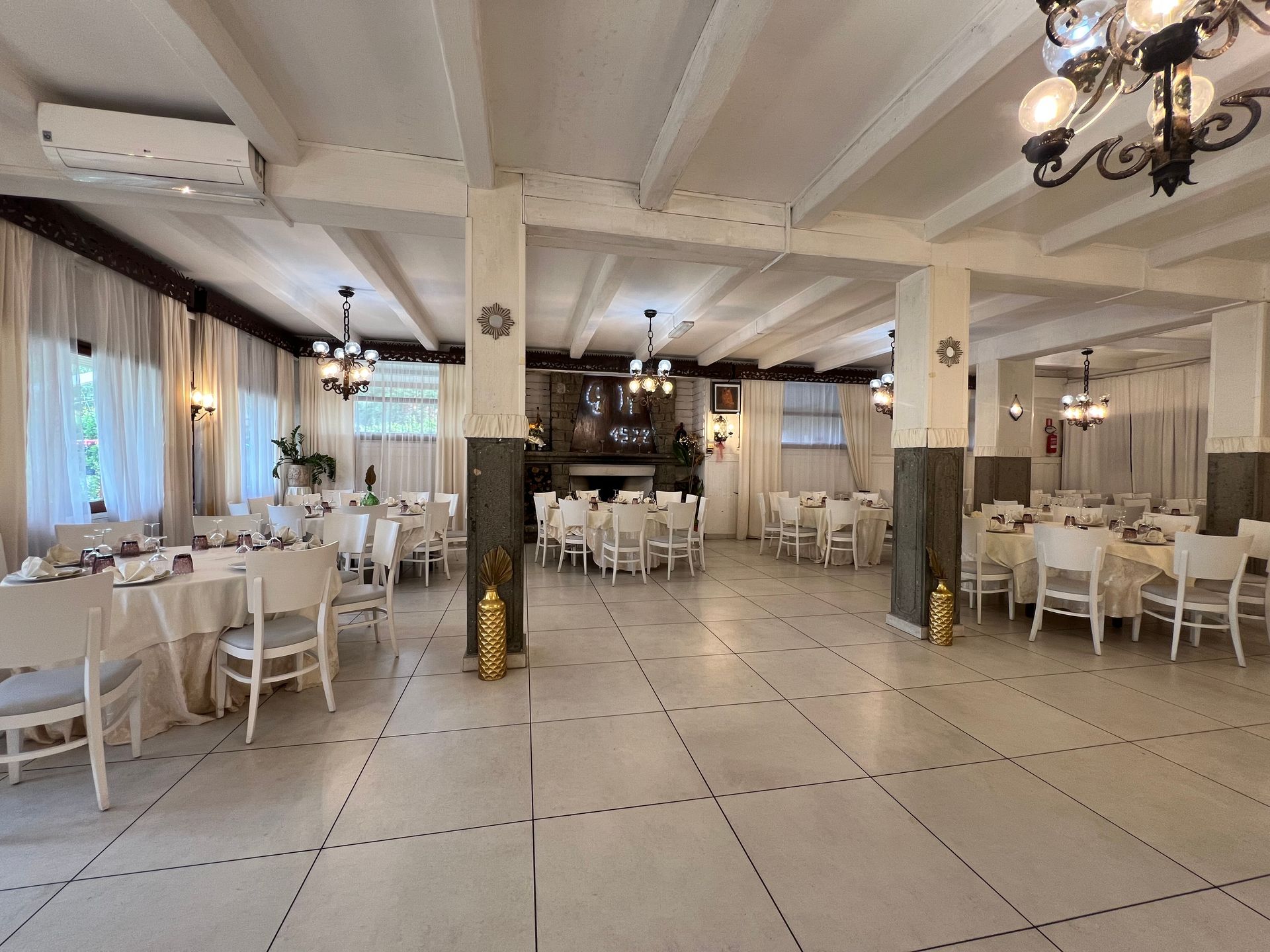 Sala da pranzo con tavoli e sedie bianchi, lampadari e pavimento in piastrelle di marmo.