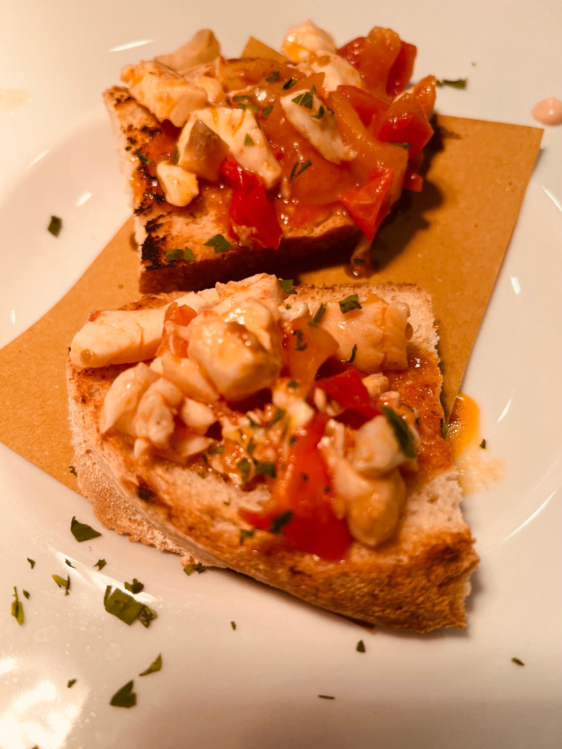 Due fette di pane tostato condite con formaggio bianco, pomodori rossi ed erbe aromatiche, su un foglio di carta marrone.