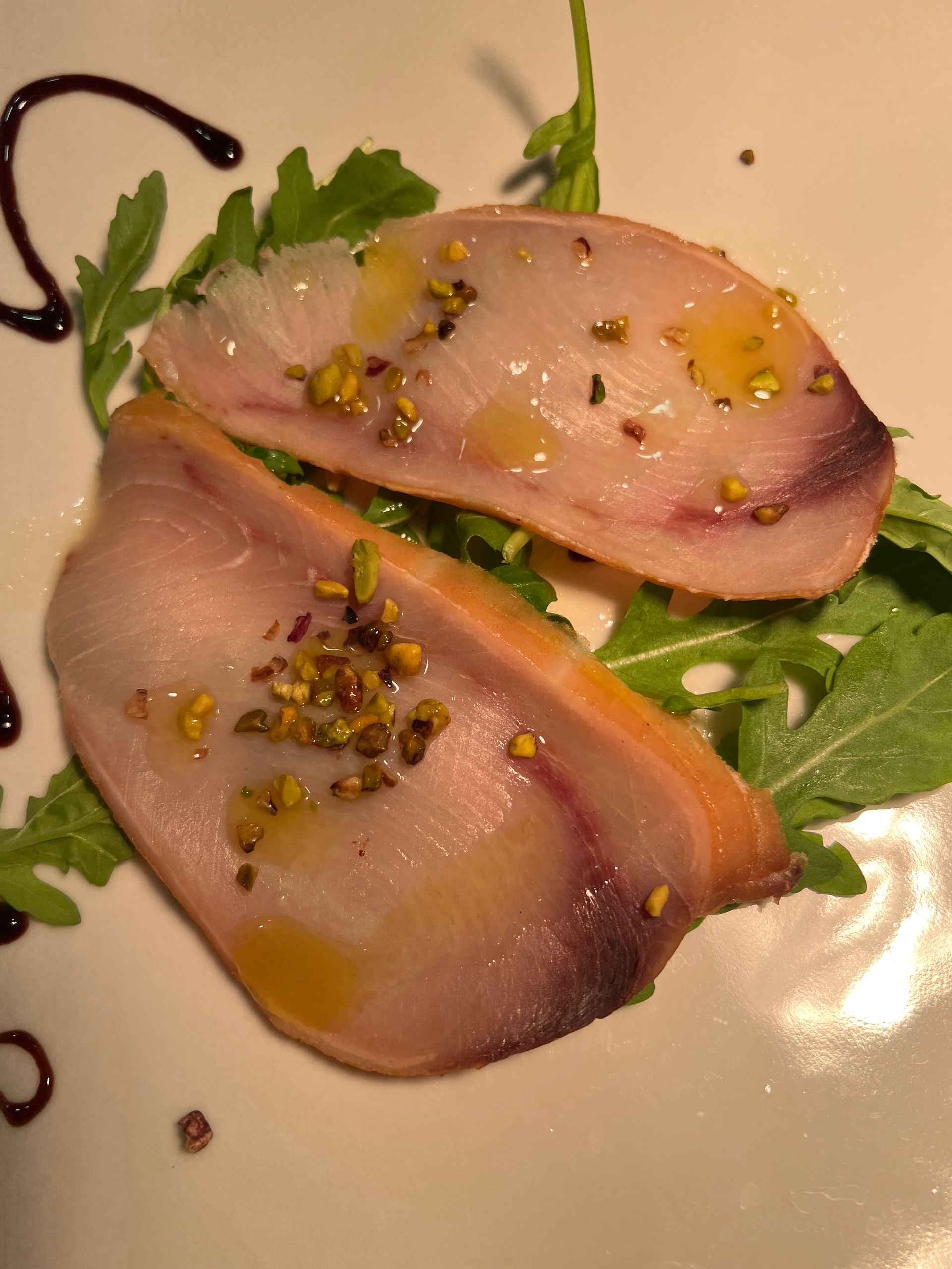 Due fette di carpaccio di pesce, condite con un filo d'olio, su rucola e guarnite con pistacchi.