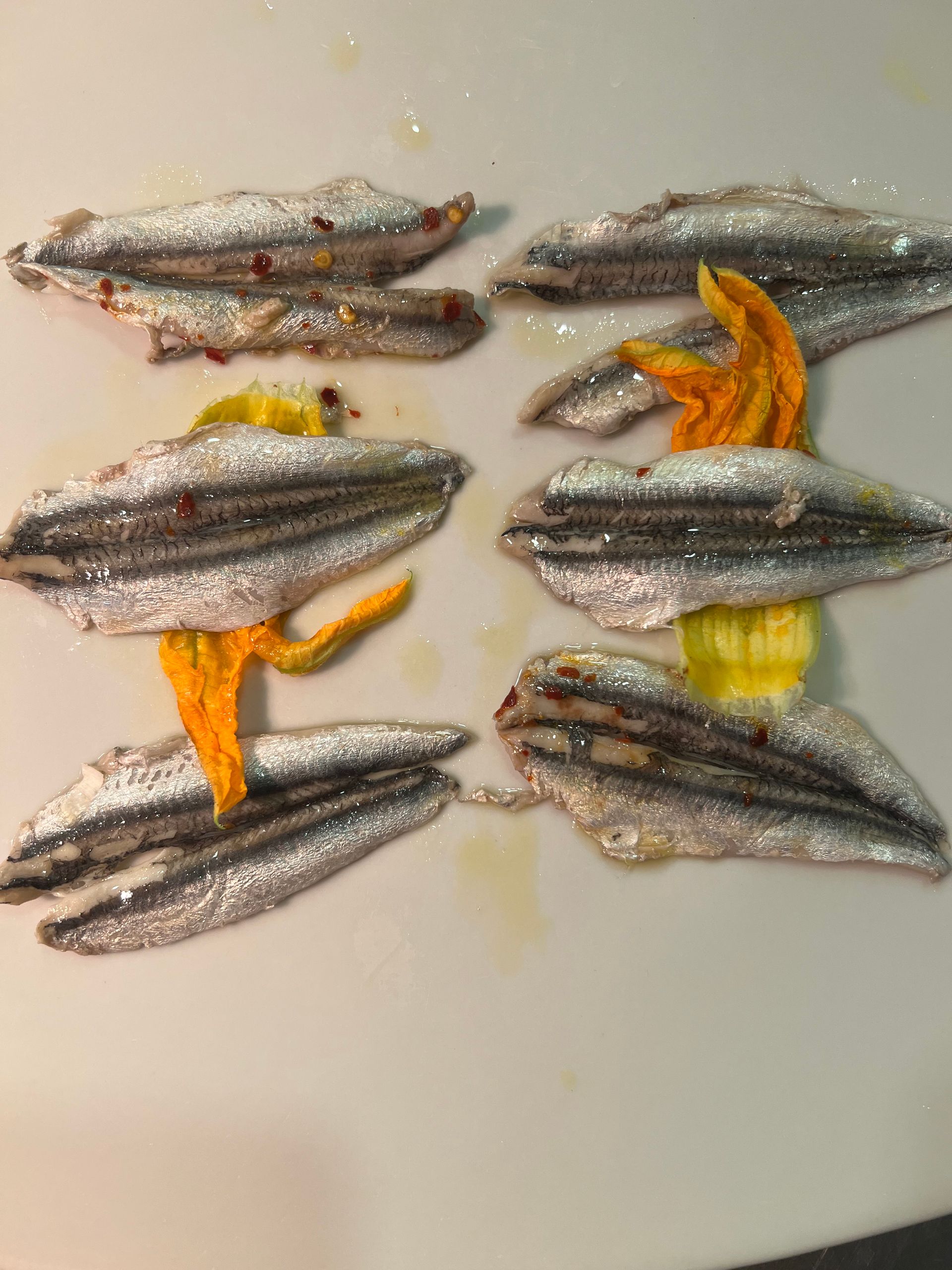 Otto filetti di acciuga disposti su una superficie bianca, con oggetti gialli in mezzo.