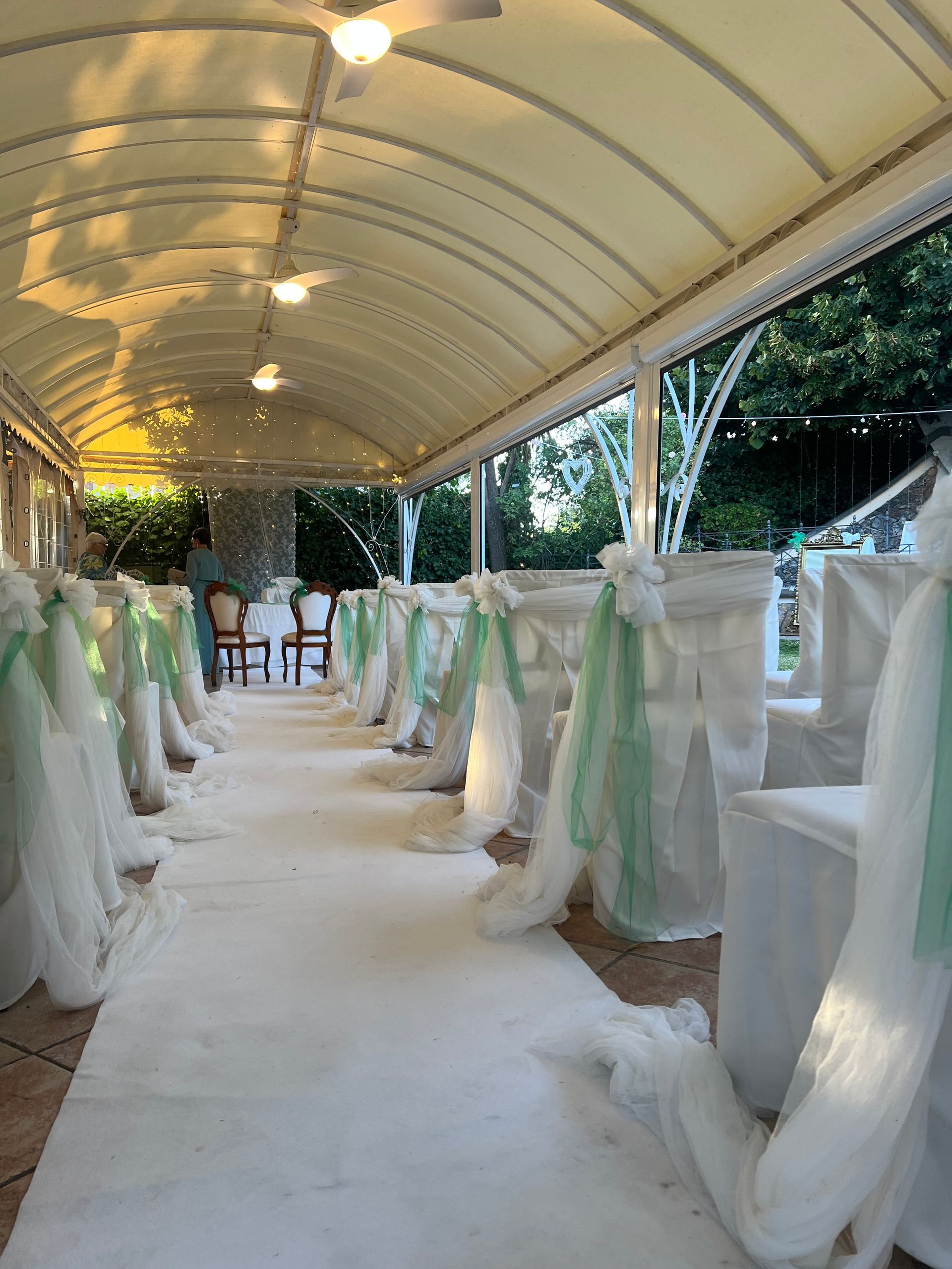 Navata nuziale sotto un baldacchino con tappeto bianco, sedie decorate e tessuto trasparente verde e bianco.