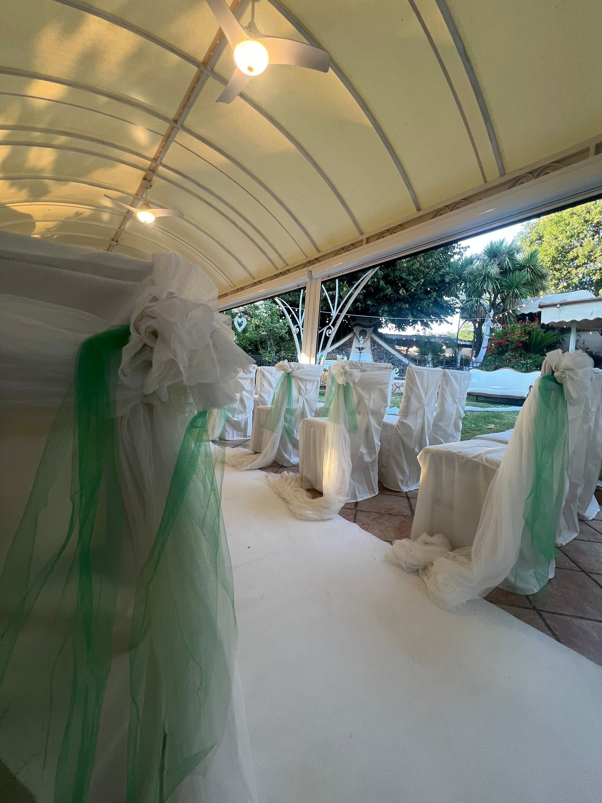 Ricevimento di nozze con decorazioni bianche e verdi sotto un'area esterna coperta.