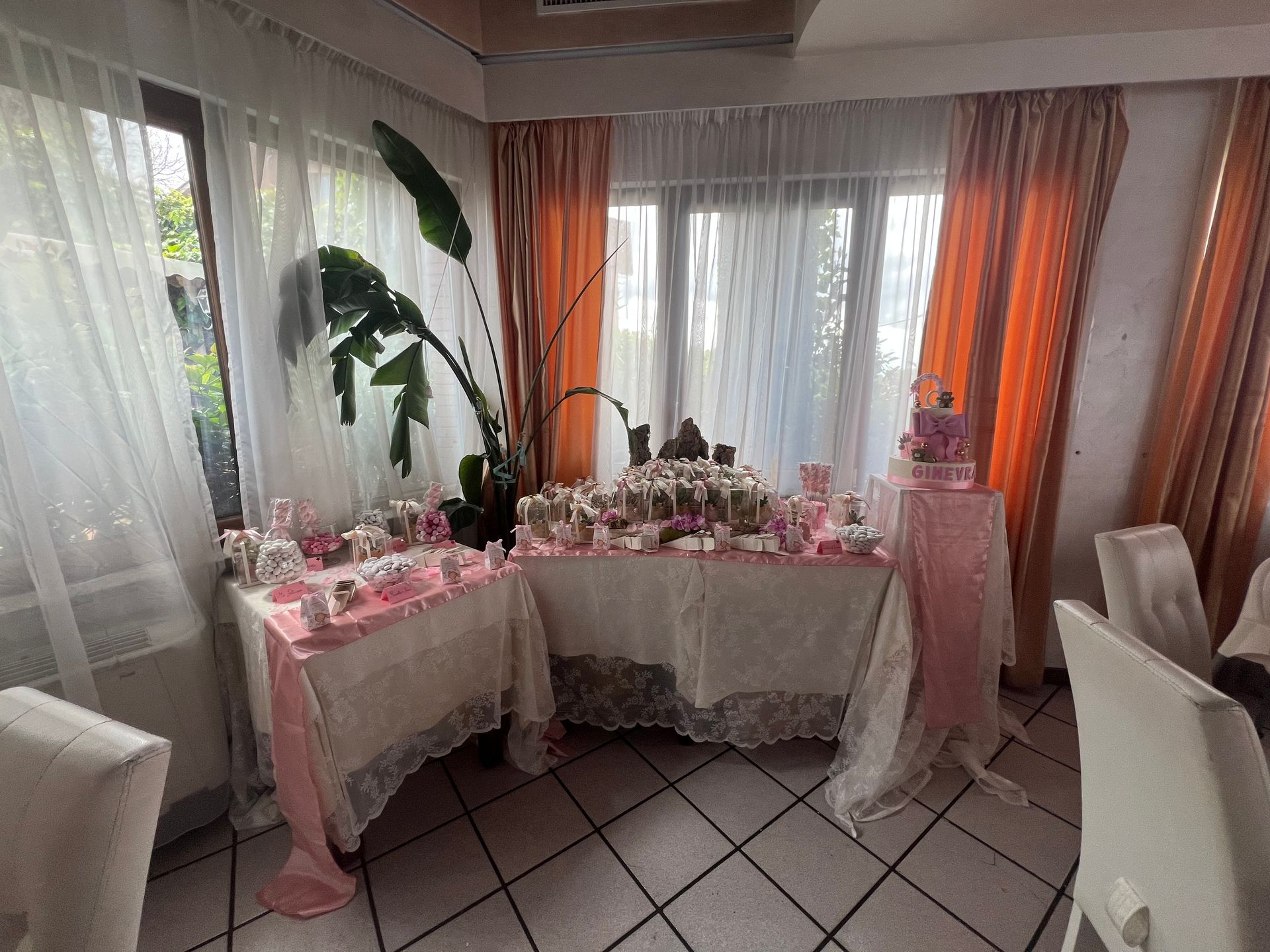 Un tavolo da dessert decorato con tovaglie rosa e bianche e dolcetti, accanto a una finestra.