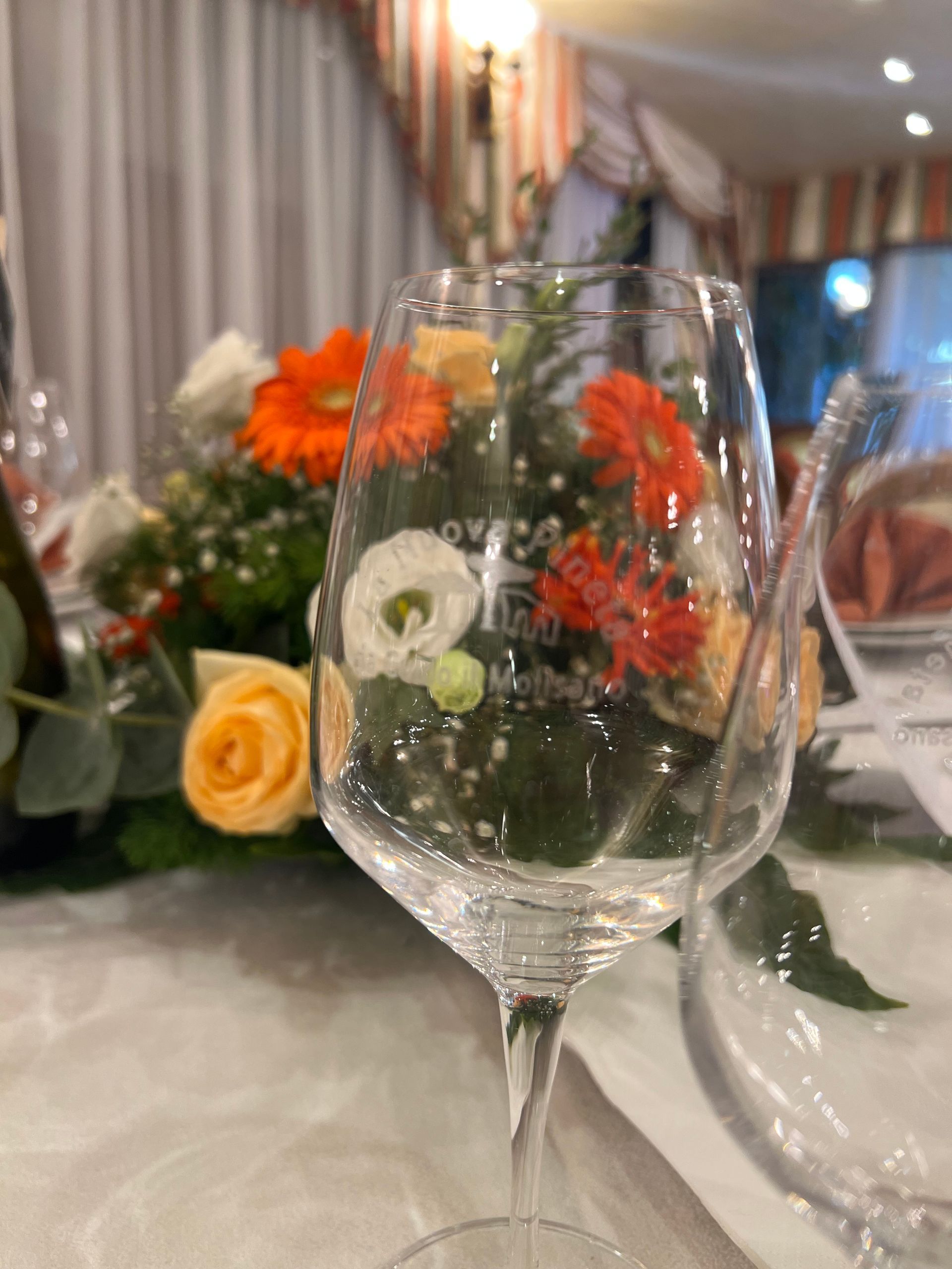 Bicchiere da vino con fiori sullo sfondo, posto su un tavolo durante una cena.