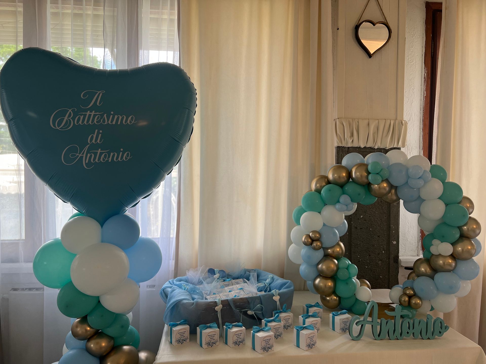 Decorazioni con palloncini blu e oro per un battesimo, tra cui un palloncino a forma di cuore, una ghirlanda e piccole scatole regalo.