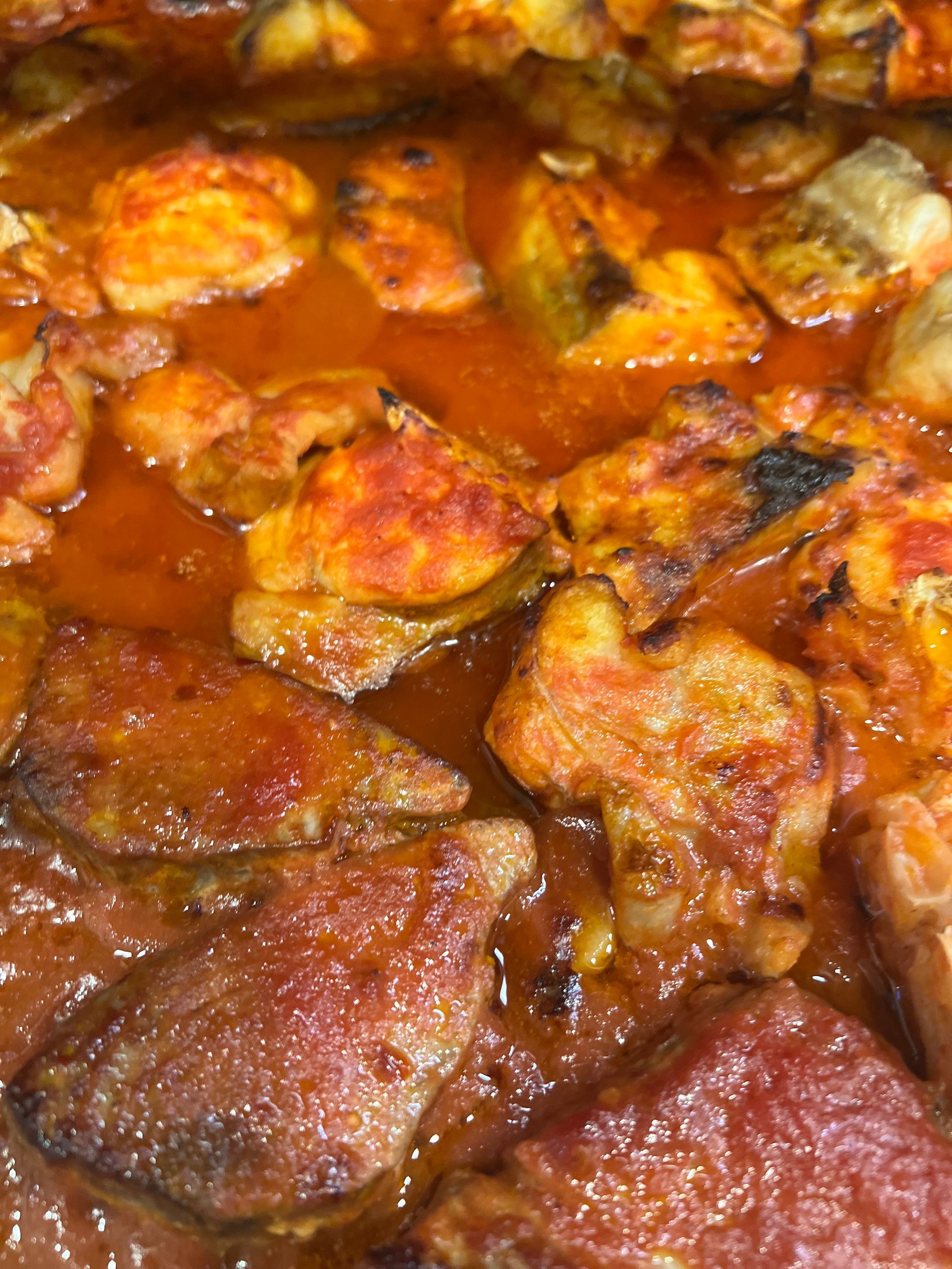 Pezzi di pollo in una salsa densa, rosso-arancio, probabilmente uno stufato o un brasato.