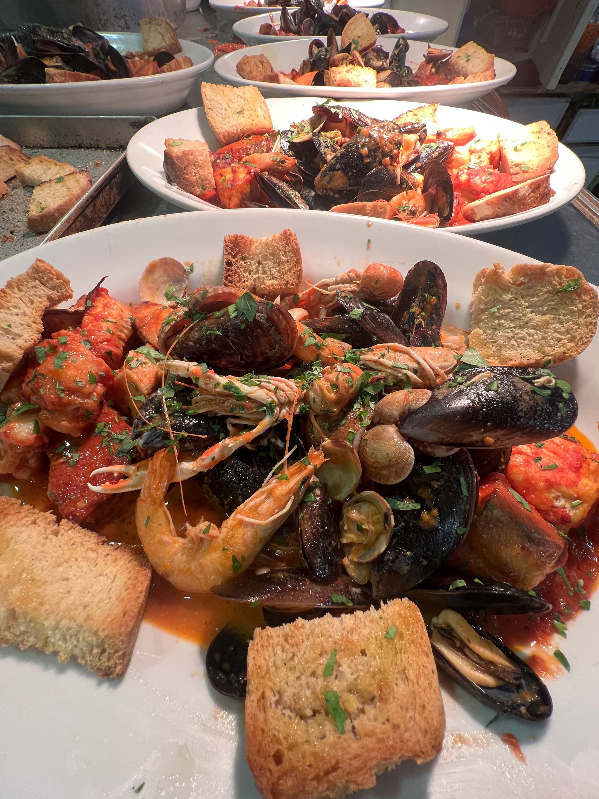 Stufato di frutti di mare con cozze, gamberi e crostini su piatti bianchi.