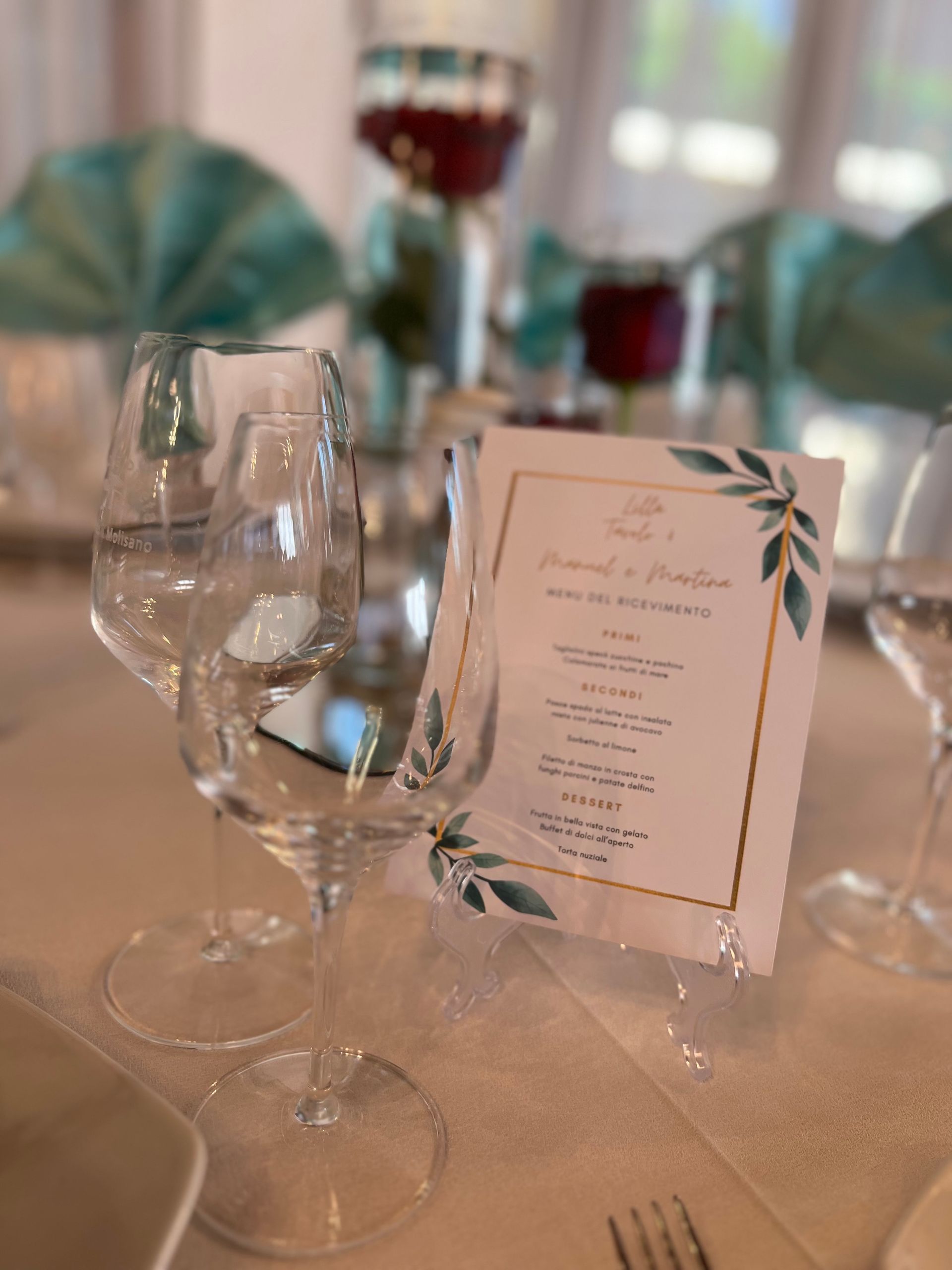 Apparecchiatura della tavola con bicchieri da vino, menù e centrotavola floreale; combinazione di colori verde acqua e bianco.