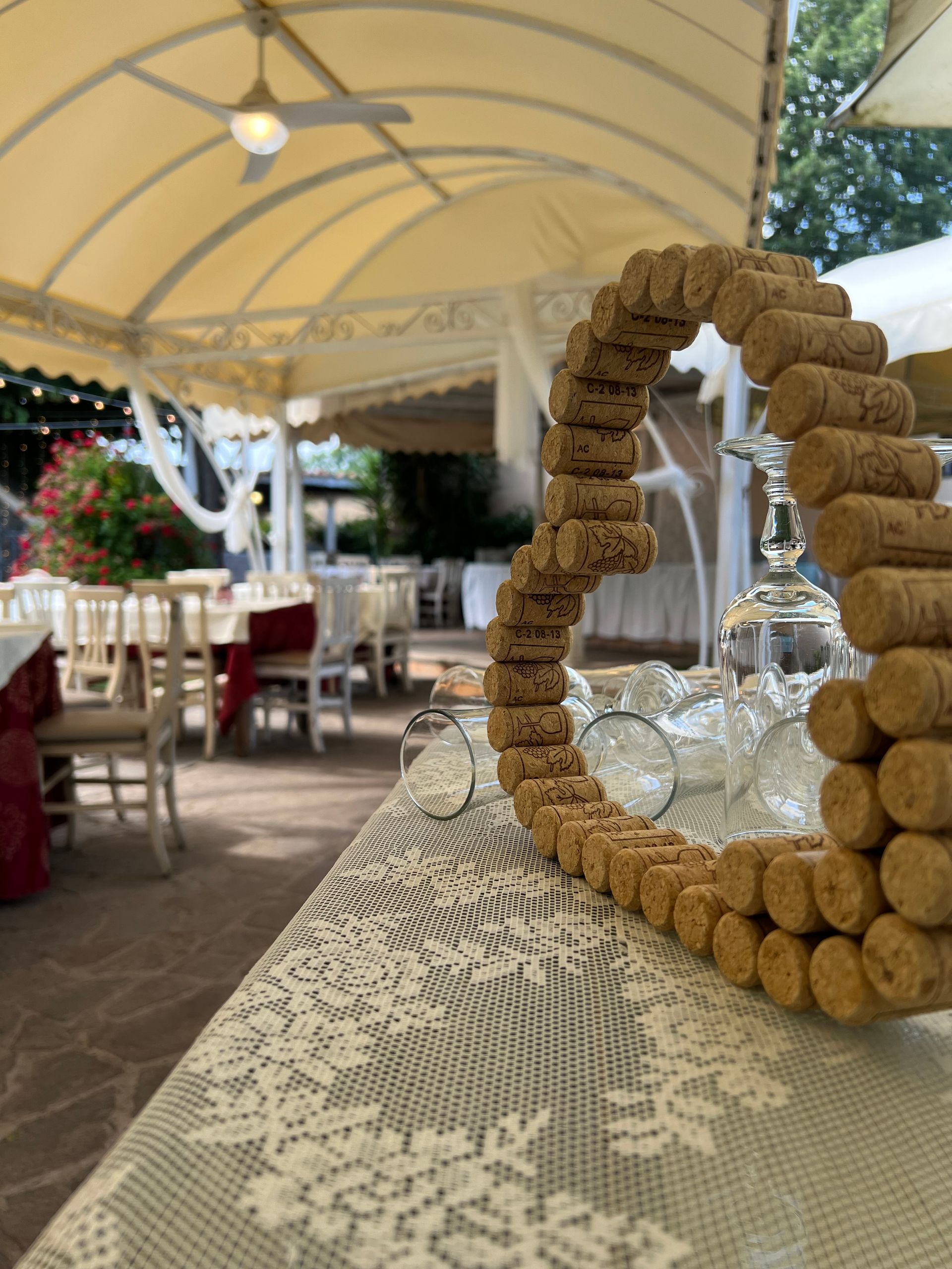 Una scultura a forma di cuore realizzata con tappi di sughero è posta su un tavolo ricoperto di pizzo, con un ristorante sullo sfondo.